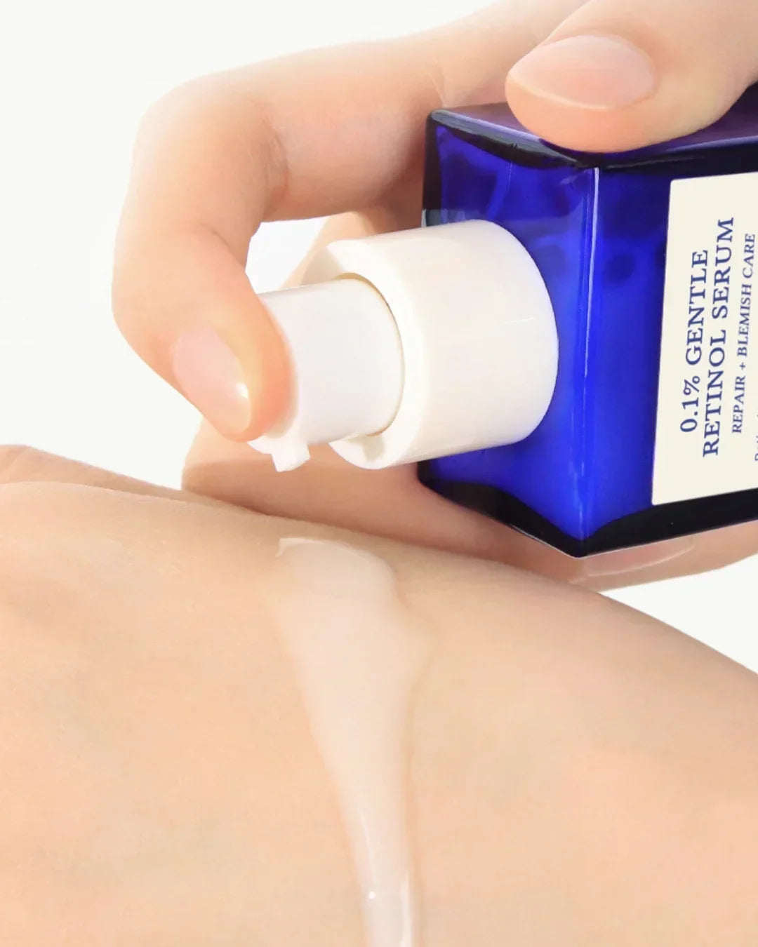 Close-up of hand dispensing 0.1% gentle retinol serum from blue bottle onto skin
