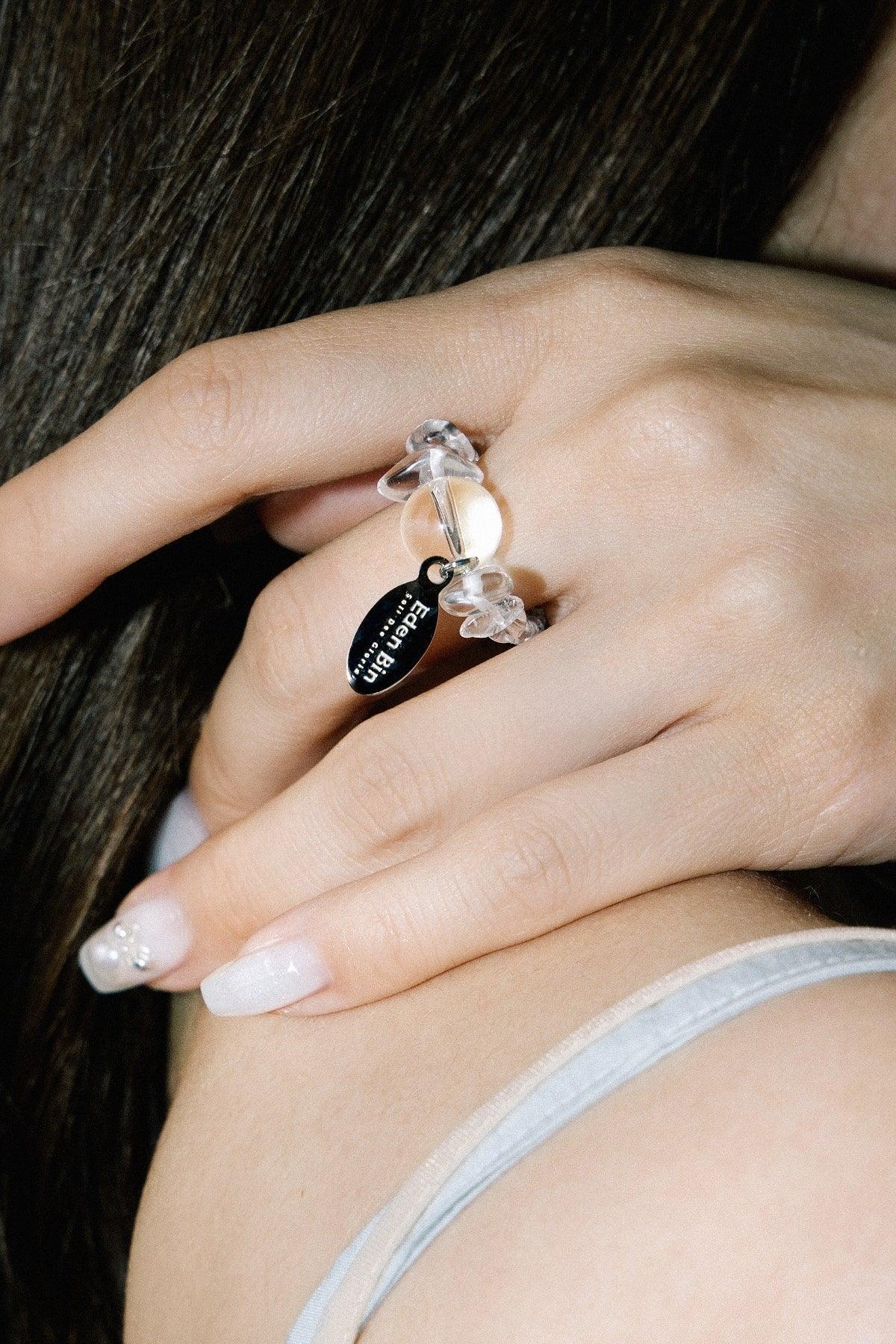 Close-up of hand wearing a transparent beaded ring with a black pendant on shoulder