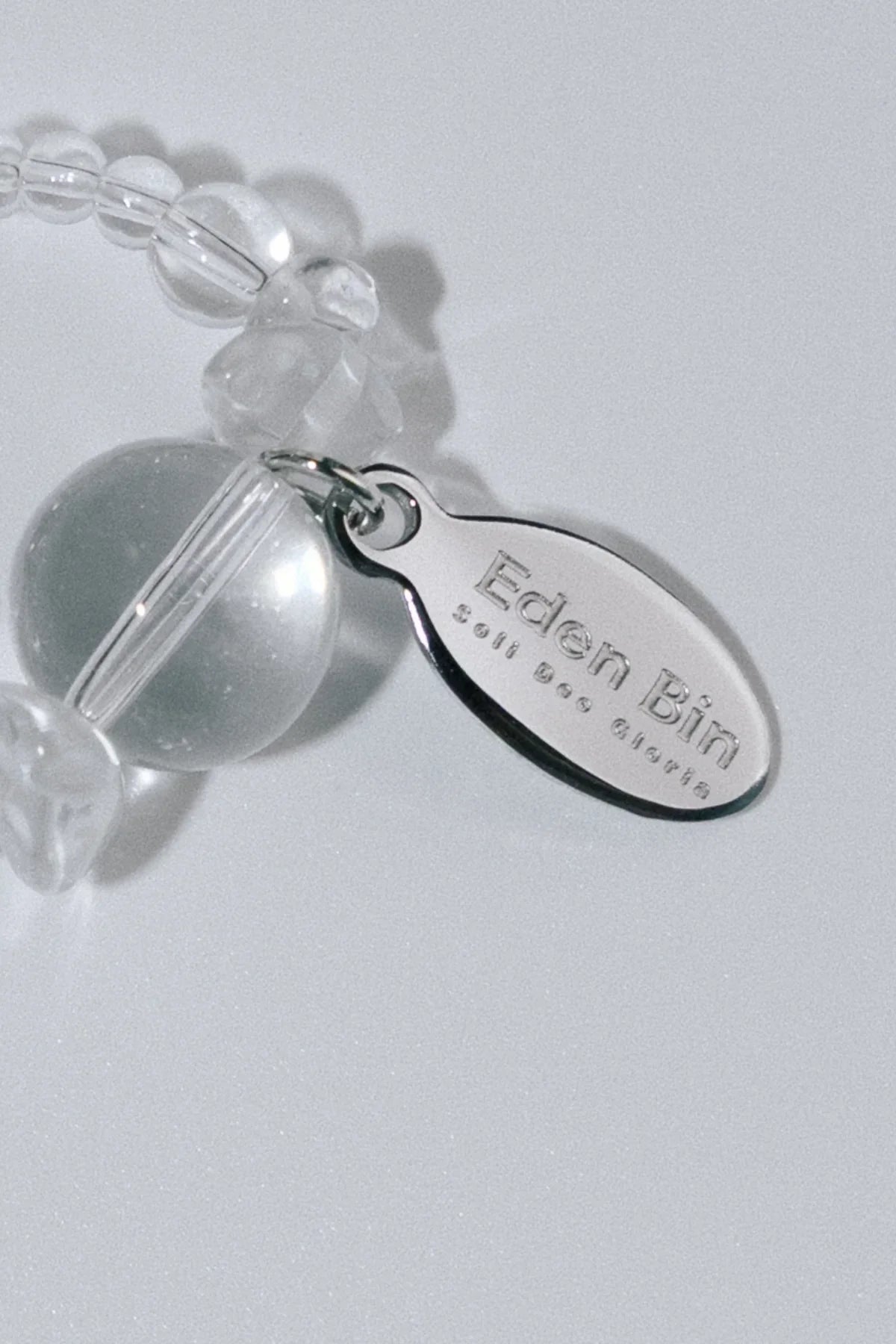 Close-up of clear bead ring with silver oval tag engraved Eden Bin Soft Dog Charoite