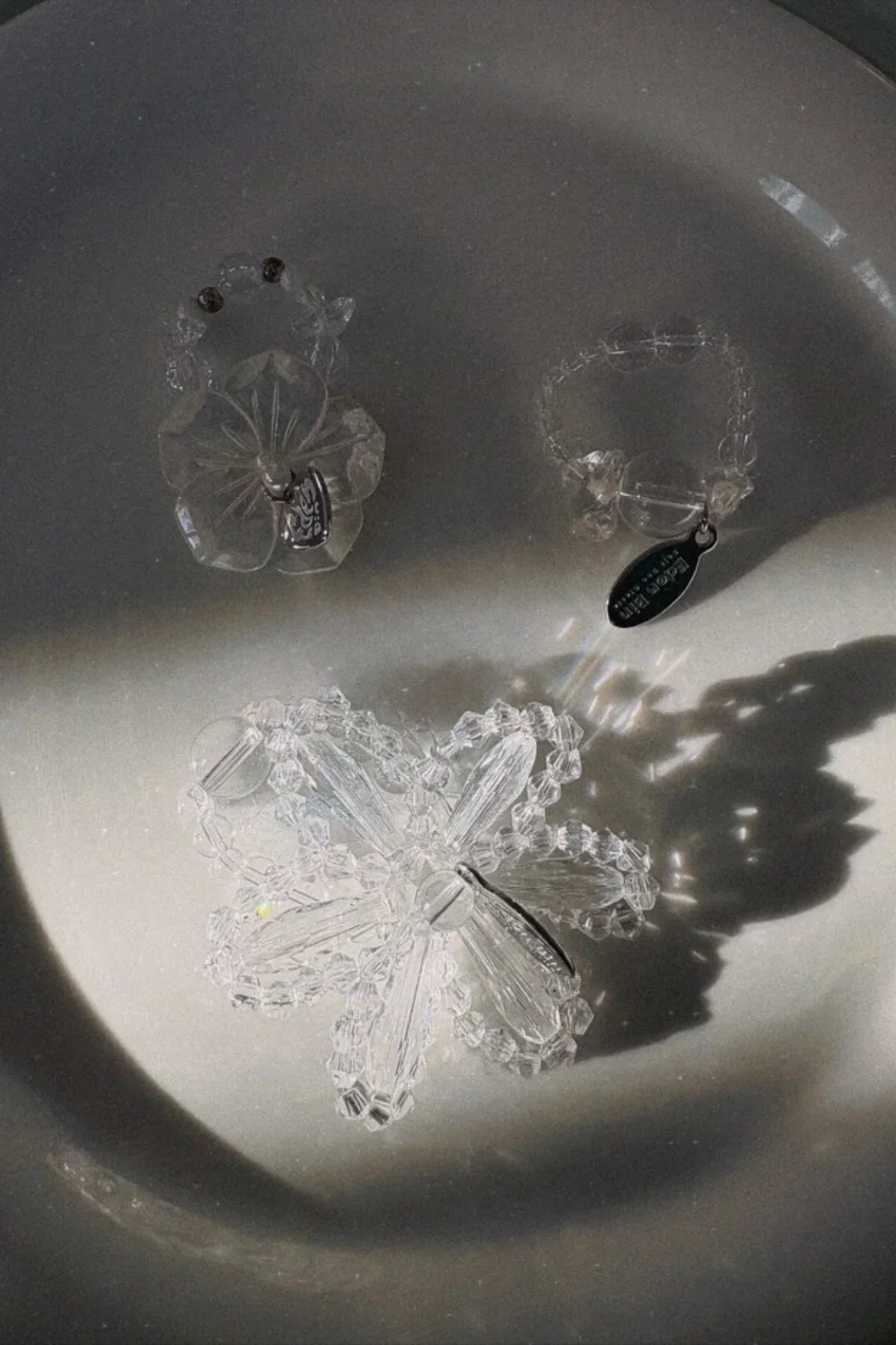 Three clear beaded rings with flower and round designs casting shadows on a white surface