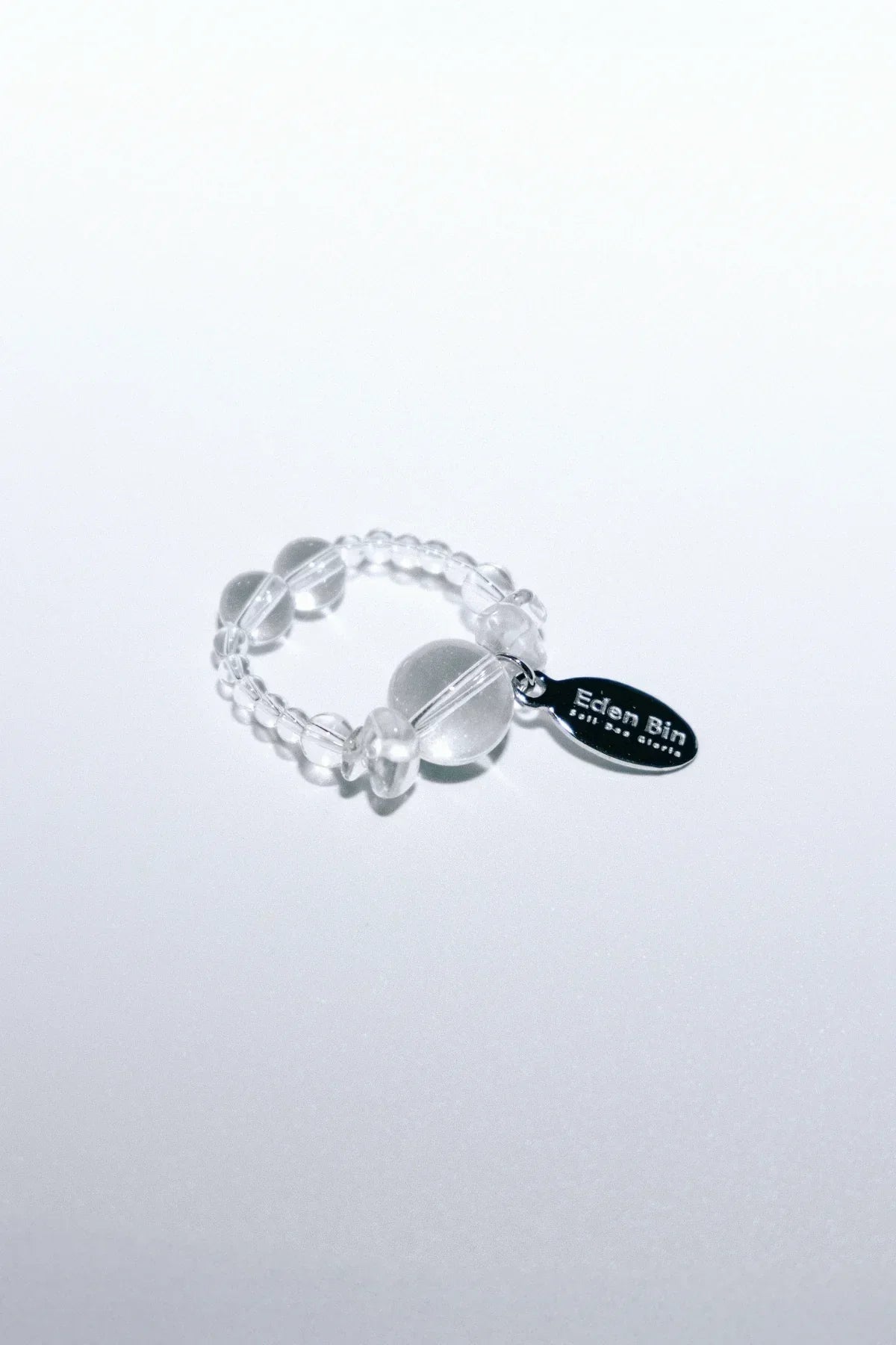 Clear beaded ring with a silver Eden Bin tag on white background