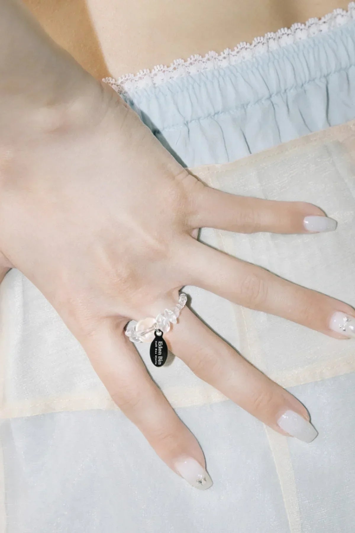 Close-up of hand wearing a clear beaded ring with a black tag, manicured nails with white polish and small star decoration