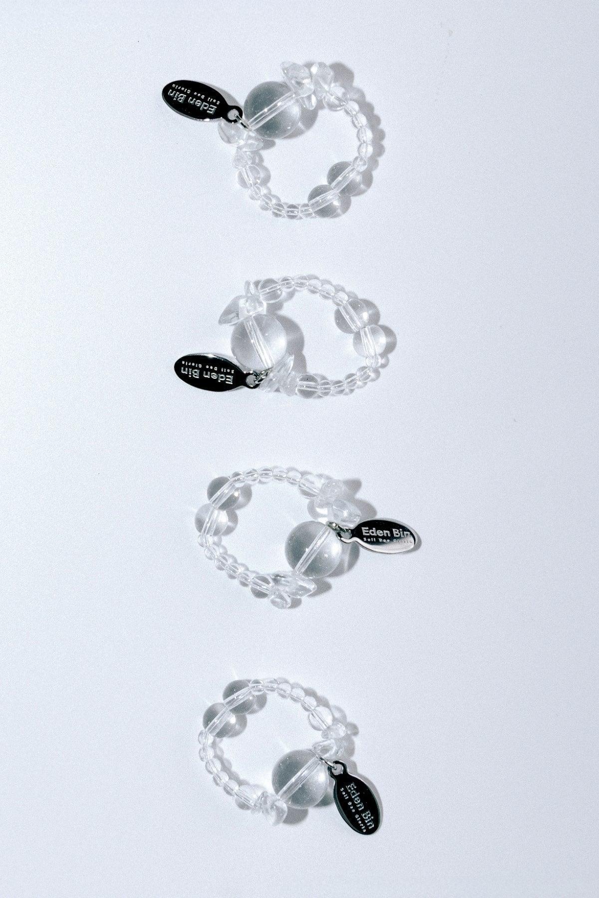 Four clear beaded rings with round center beads and Eden Bin brand tags on white background
