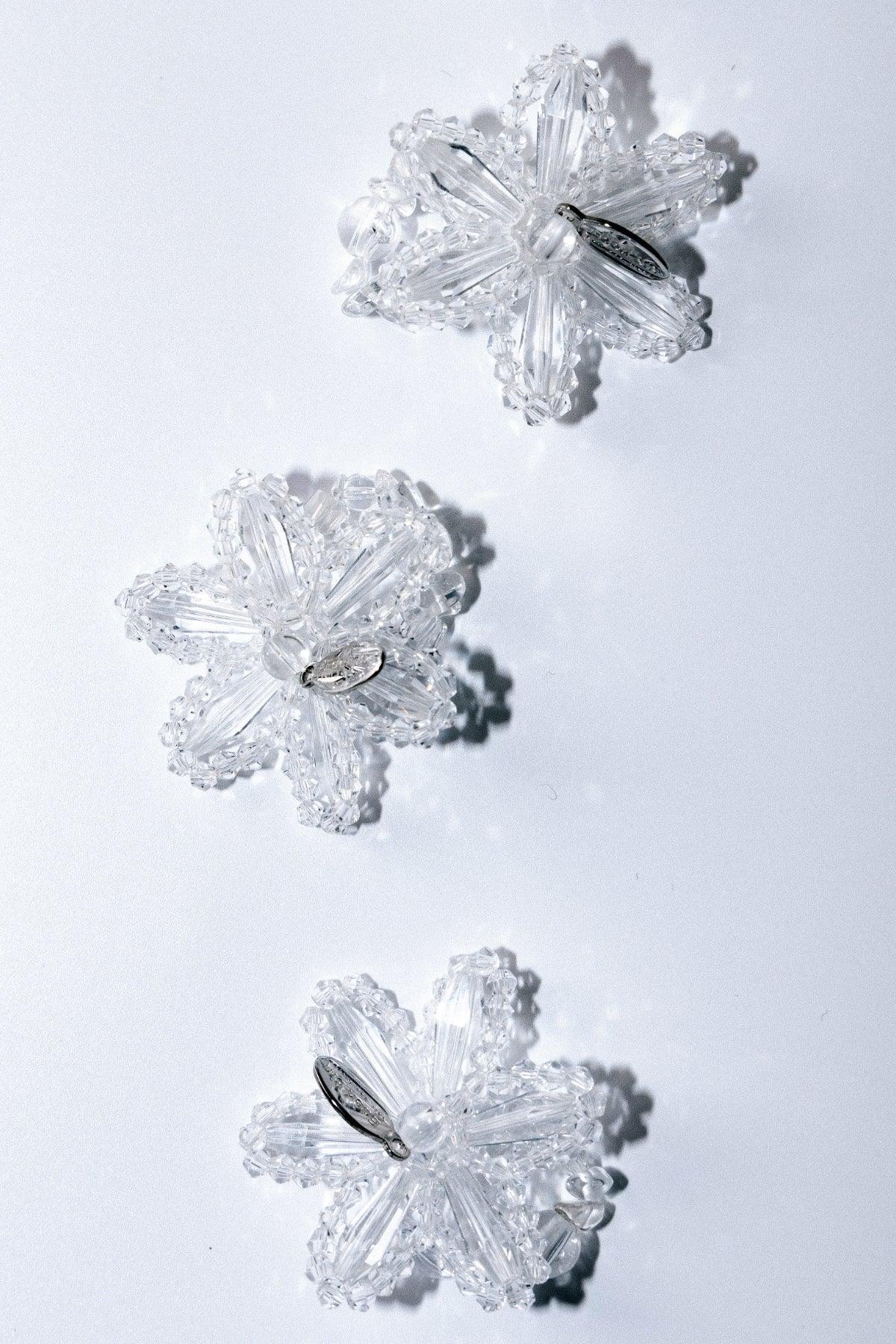 Three clear crystal flower-shaped brooches arranged on a white background casting soft shadows