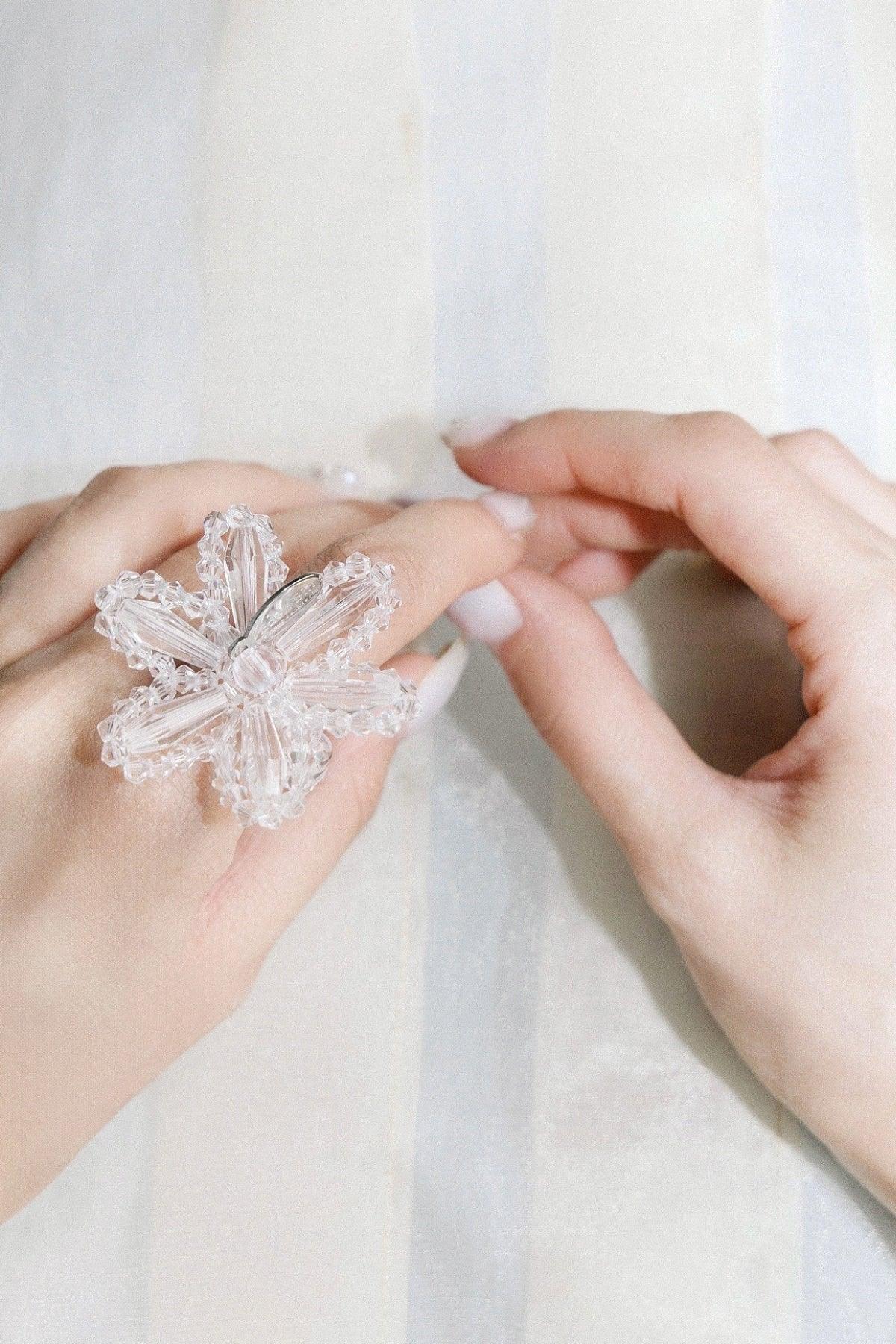 Close-up of hands with a large clear beaded flower ring on finger over soft neutral background
