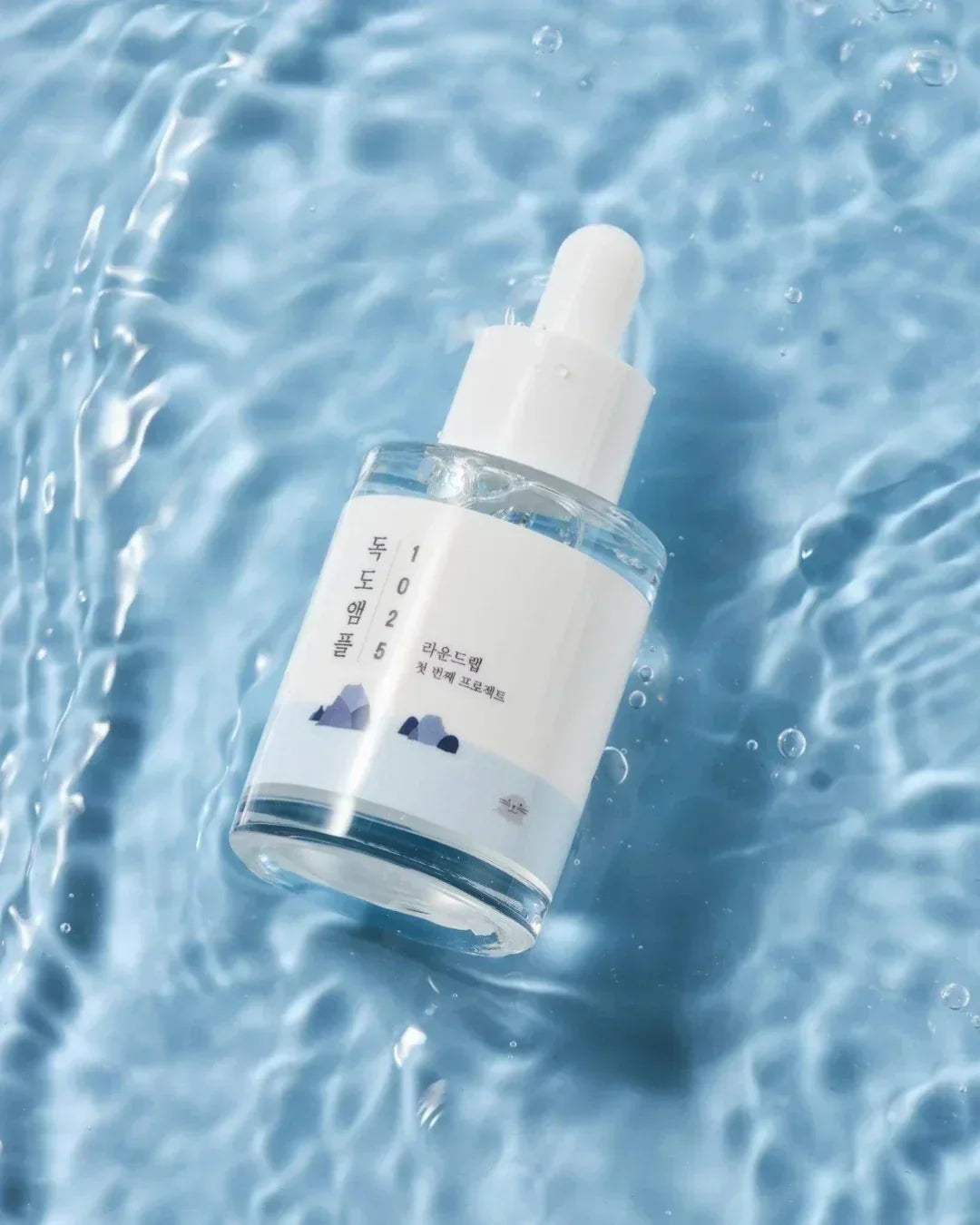 1025 Dokdo Ampule skincare serum with dropper floating on rippled blue water surface