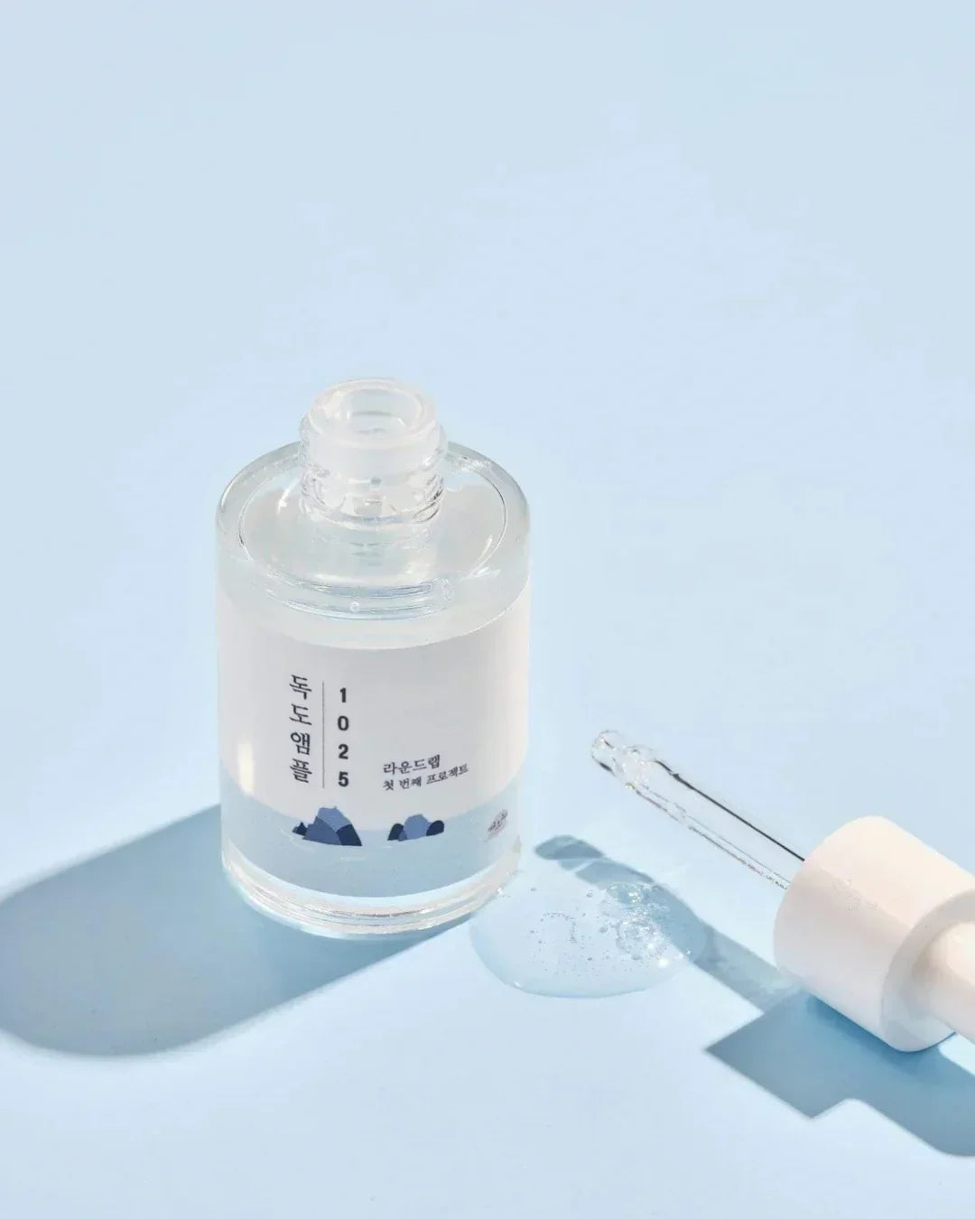 Clear skincare ampoule bottle with Korean text and dropper on light blue background