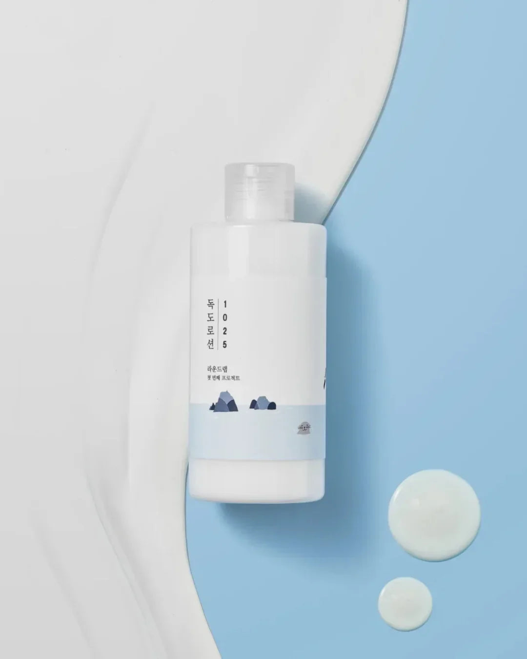 Dokdo 1025 lotion bottle on light blue and white background with lotion drops nearby