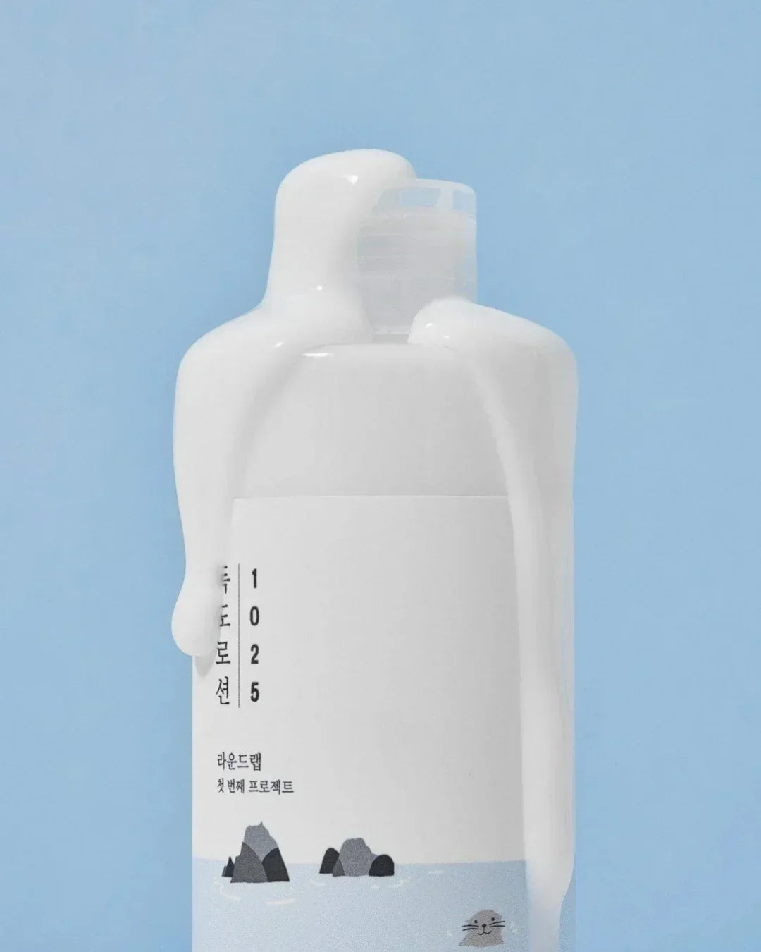 White 1025 Dokdo lotion bottle with spilled lotion on top against blue background