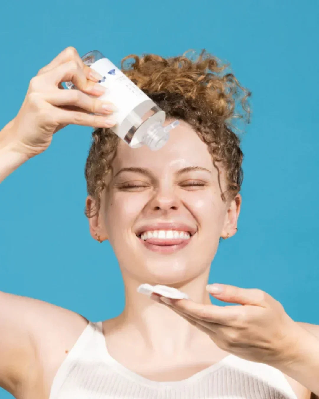 Smiling woman with curly hair applying clear toner to cotton pad against blue background