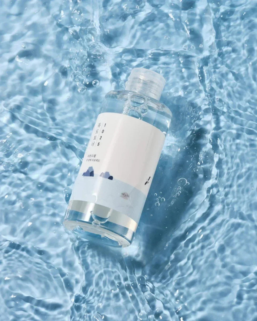Clear 1025 Dokdo toner bottle floating on rippling water surface with bubbles
