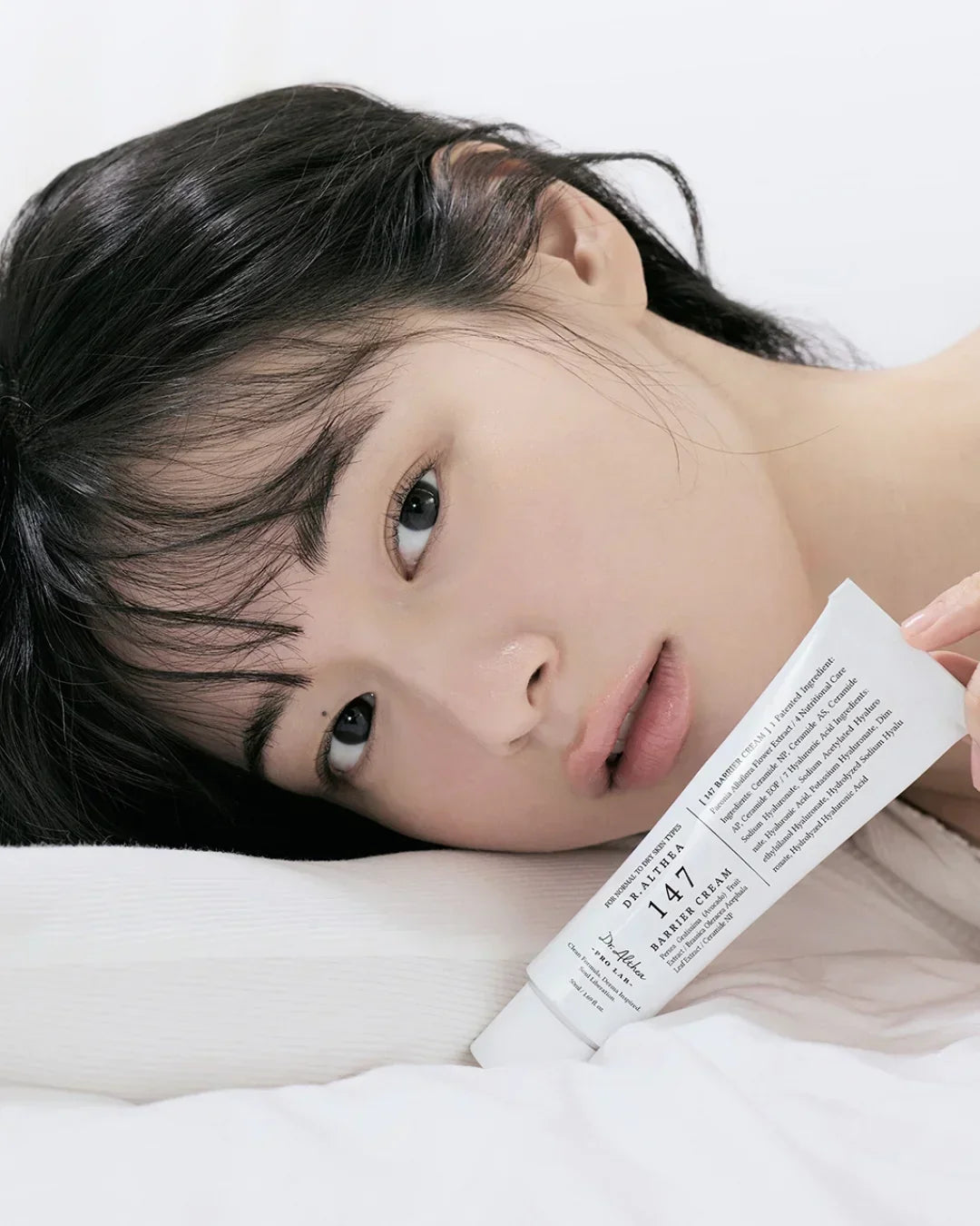 Close-up of woman with clear skin lying down holding Dr. Althea 147 Barrier Cream tube