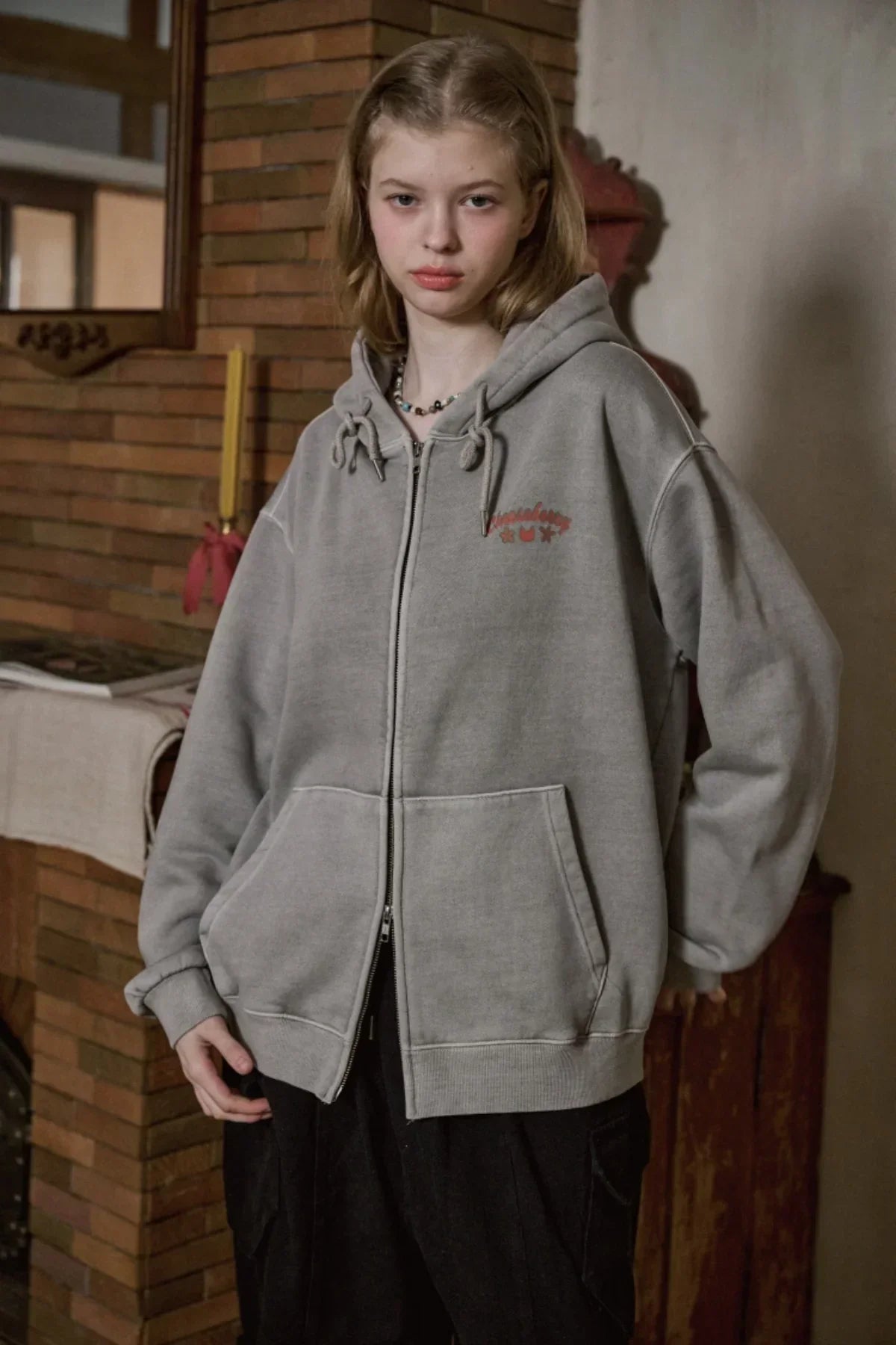Young woman wearing ghost gray hooded zip-up sweatshirt with front pockets indoors