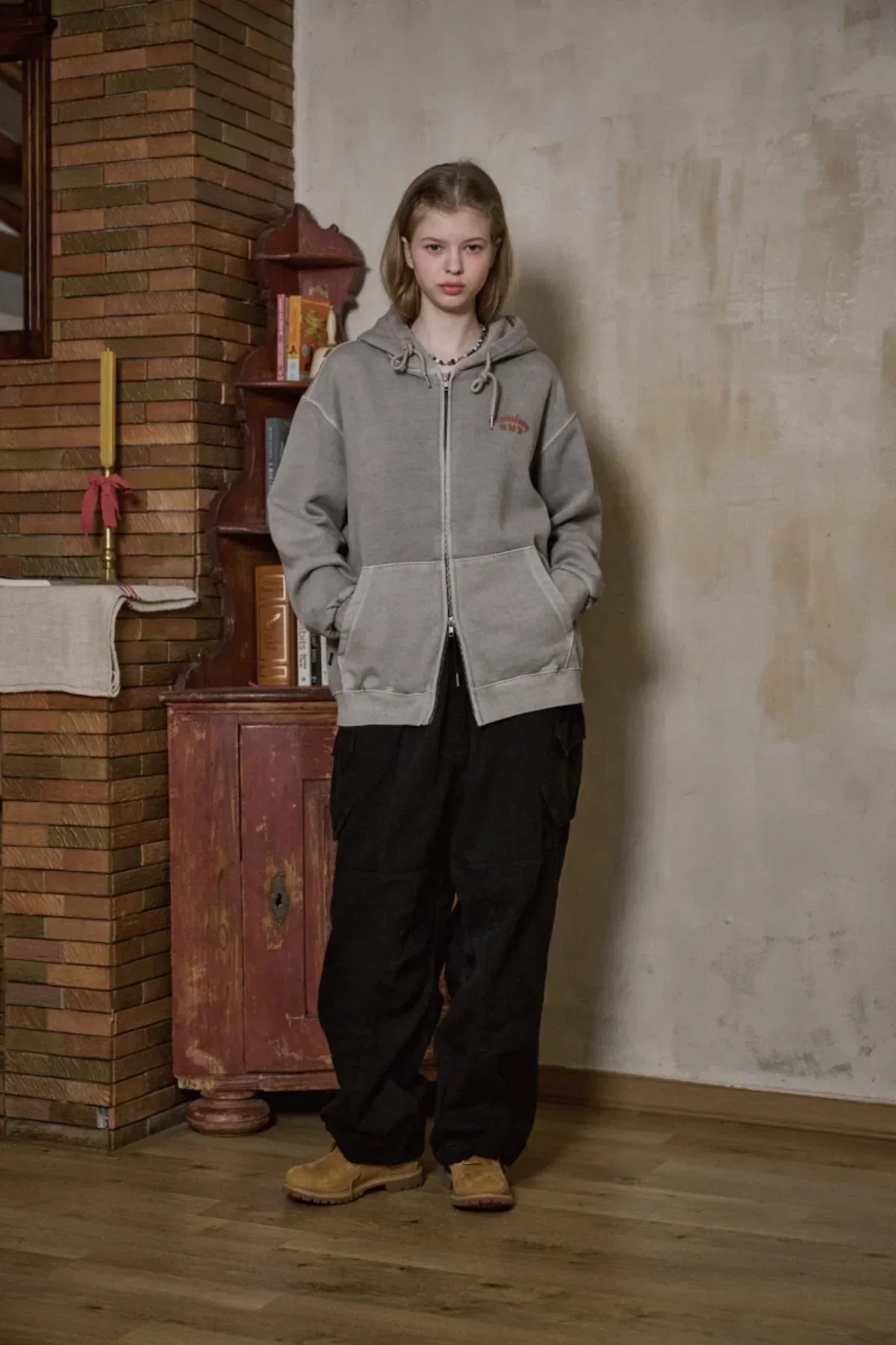 Young woman wearing ghost gray hooded zip-up sweatshirt with pockets and black cargo pants indoors