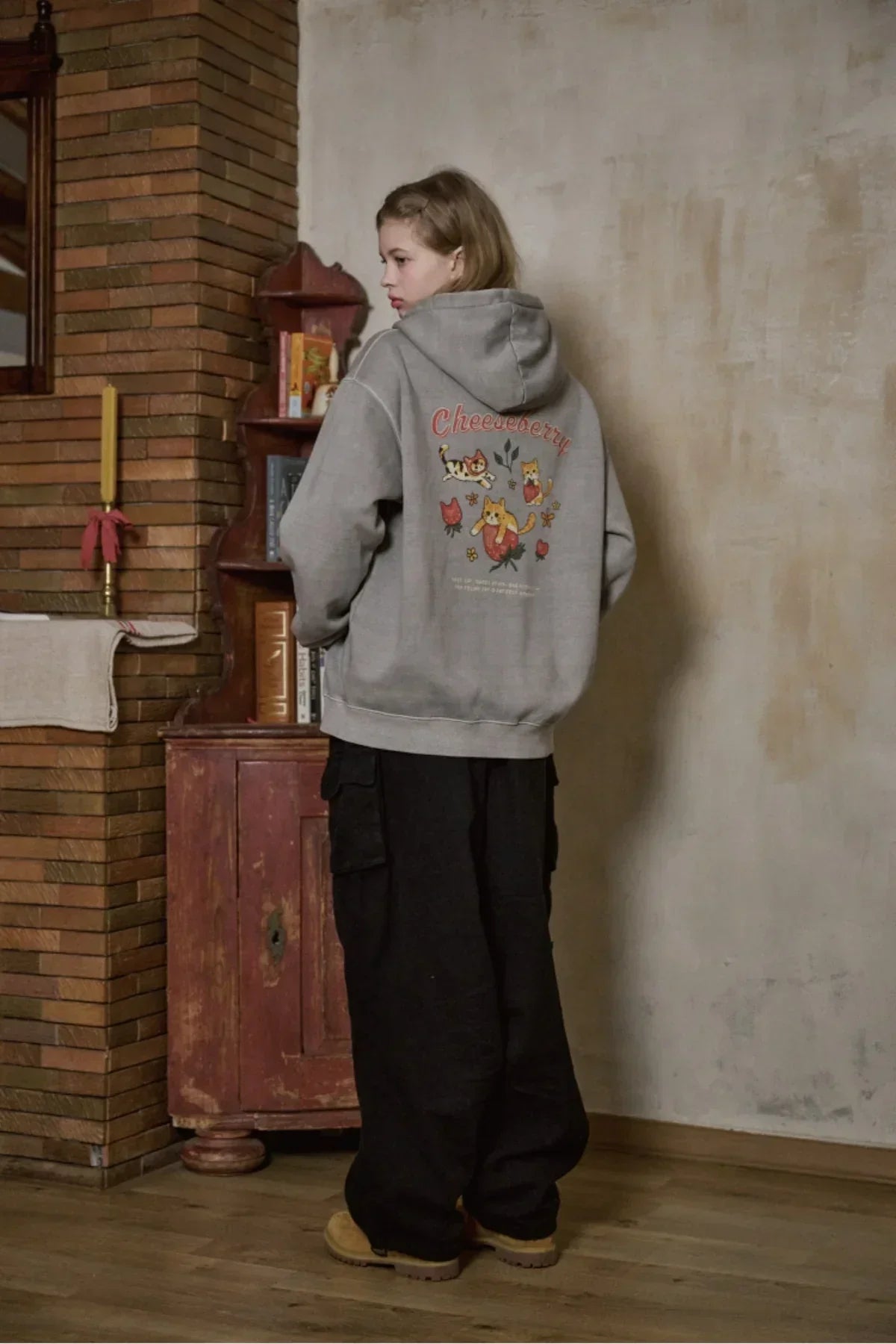 Person wearing ghost gray Cheesebberry hooded zip-up sweatshirt with cat and floral design in cozy room