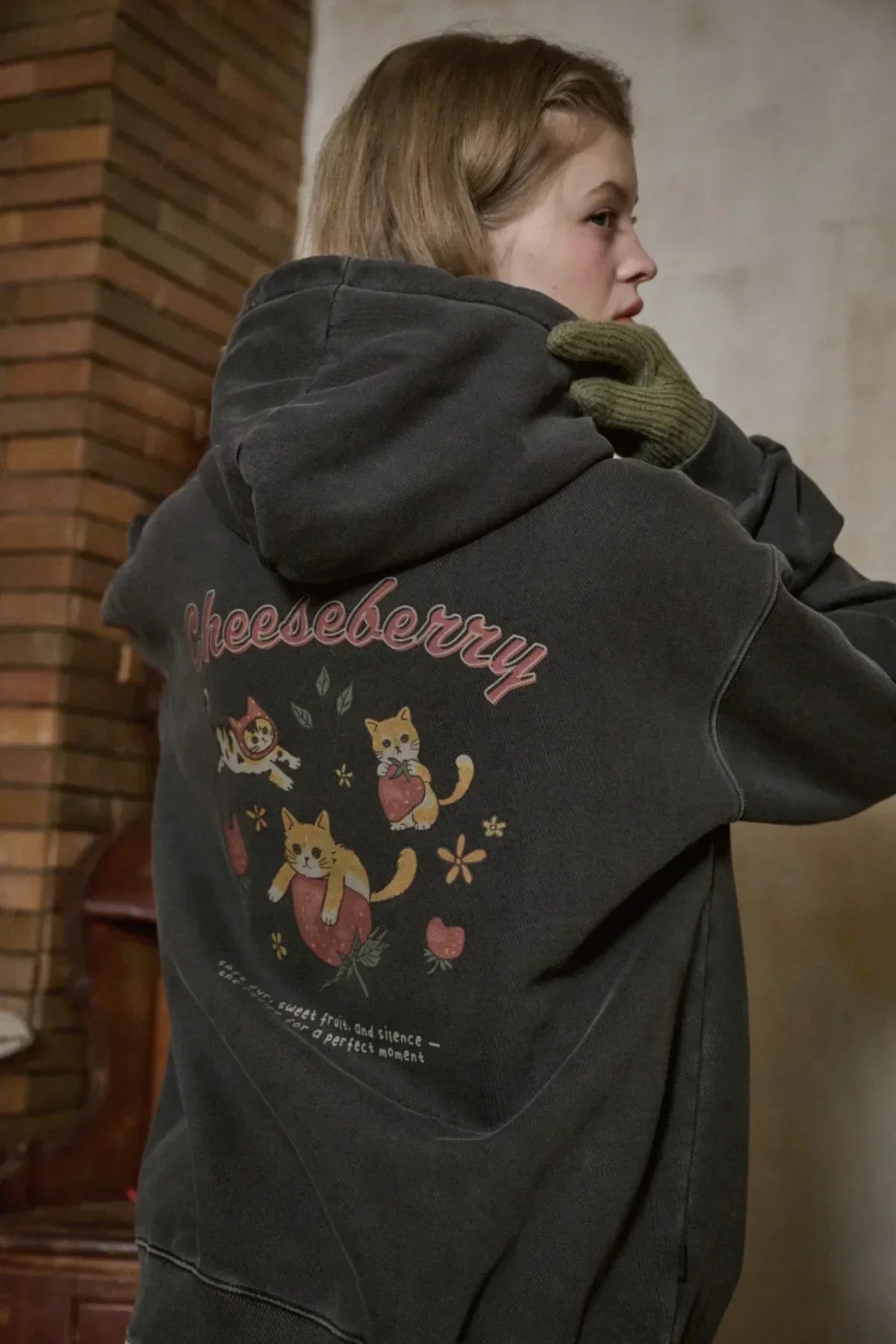 smoke black hooded zip-up sweatshirt with cheesebsrry cat and strawberry graphic on back worn by woman indoors