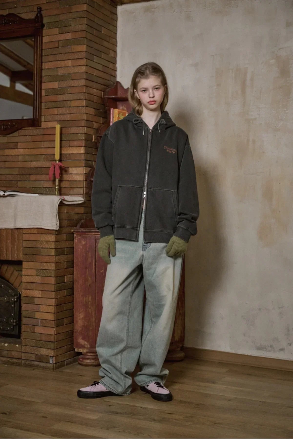 Young woman wearing smoke black zip-up hooded sweatshirt with green gloves and baggy jeans indoors