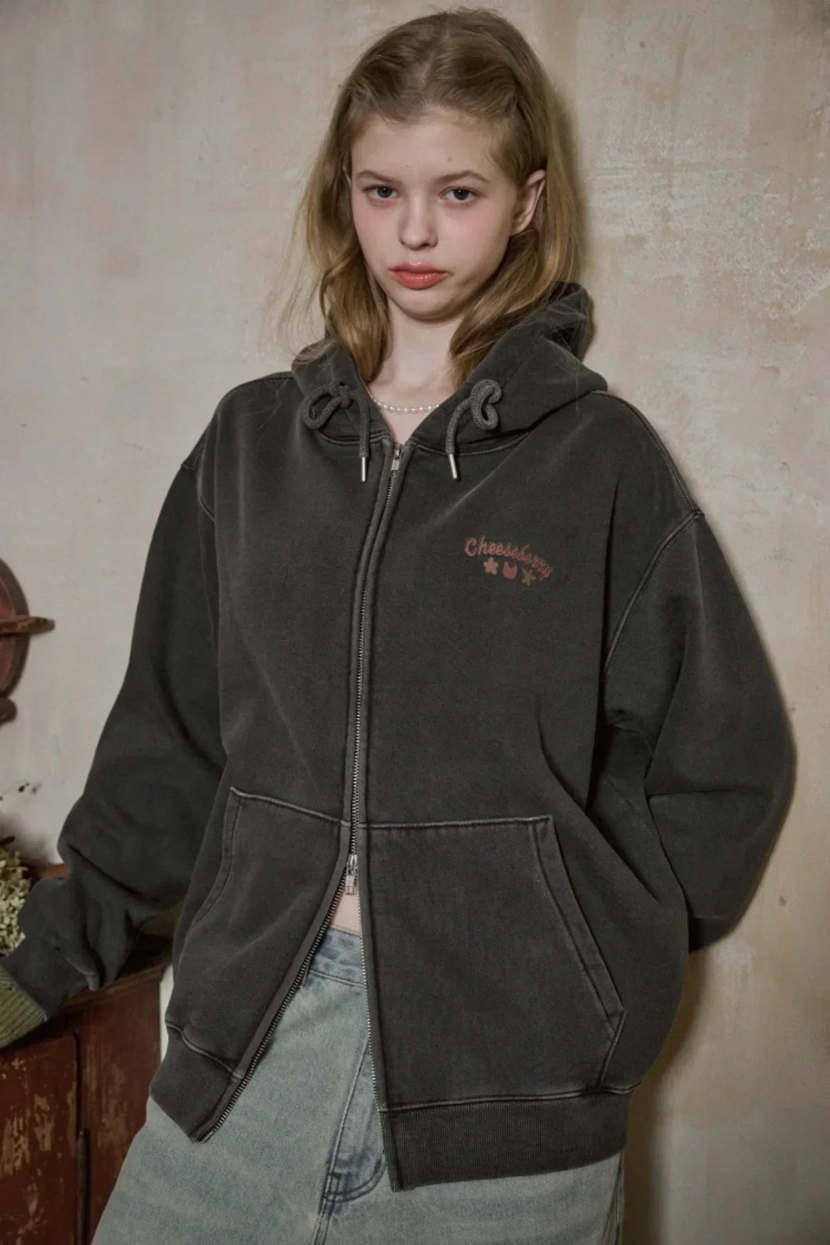 Young woman wearing charcoal hooded zip-up sweatshirt with Cheesberry logo and light washed jeans
