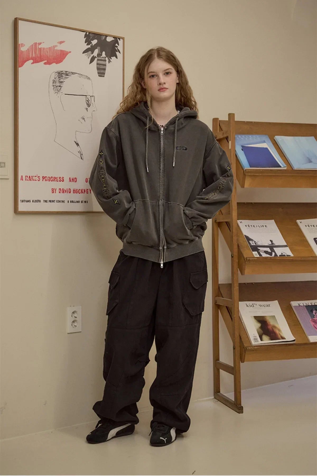 Young woman wearing dark gray hooded zip-up jacket and baggy black cargo pants in indoor studio