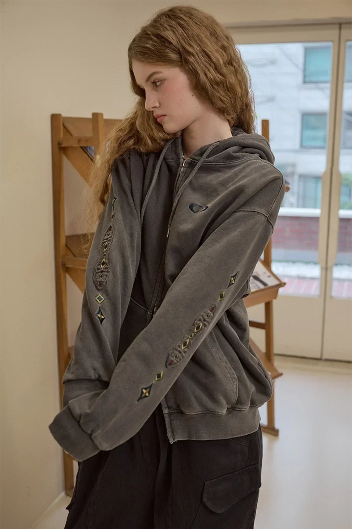 woman wearing smoke black zip-up hoodie with embroidered geometric patches on sleeves indoors