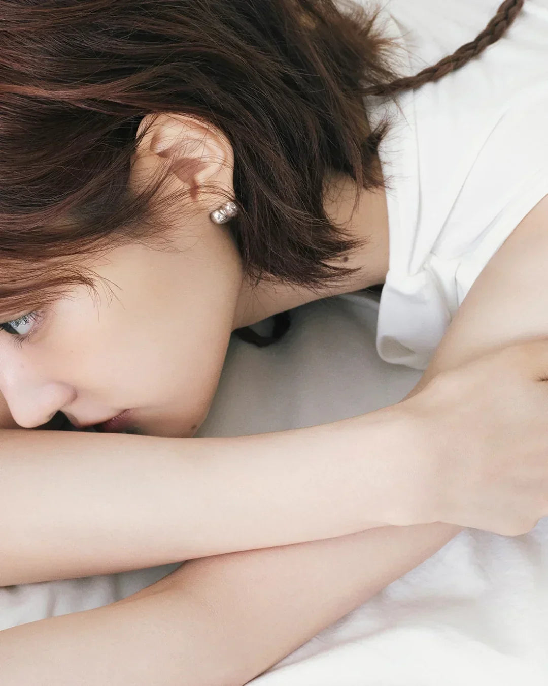 Close-up of a woman with short brown hair lying down, showcasing smooth skin and pearl earrings
