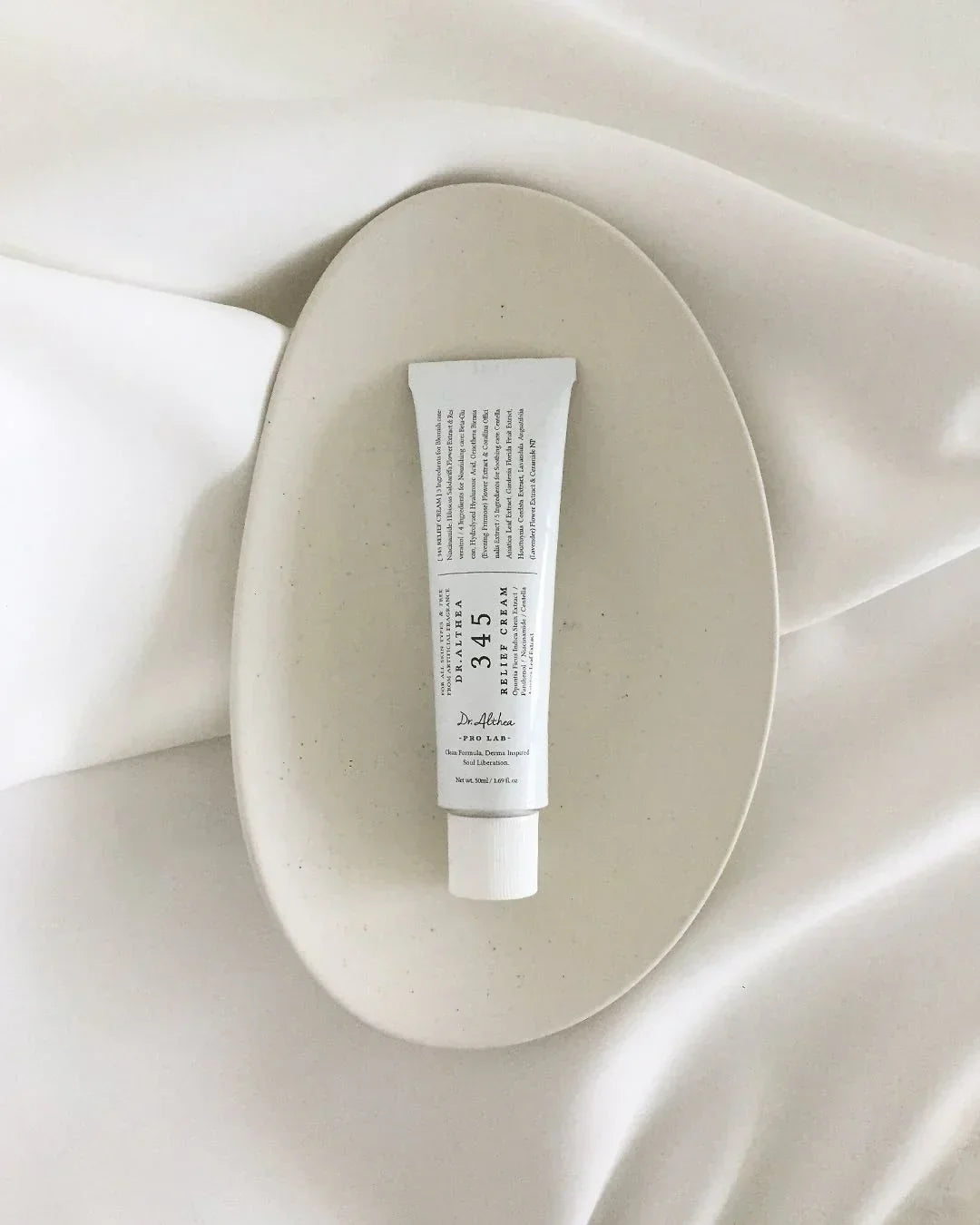 Tube of Dr. Althea 345 Relief Cream on a beige ceramic plate with white fabric background