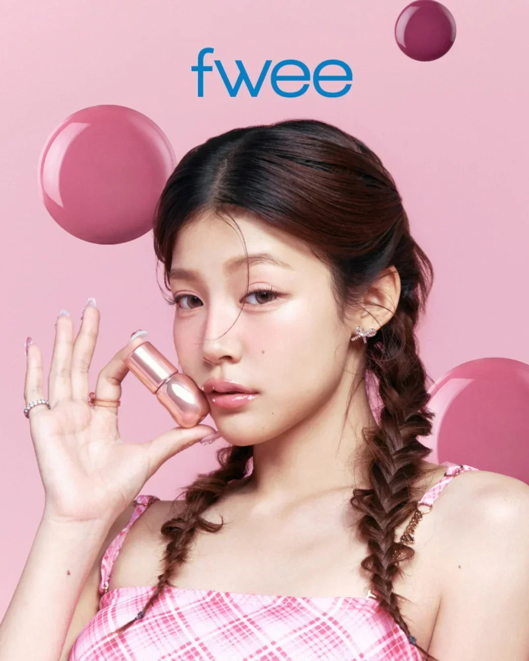 Young woman with braided hair holding pink 3D voluming gloss lip product against pink background with fwee logo