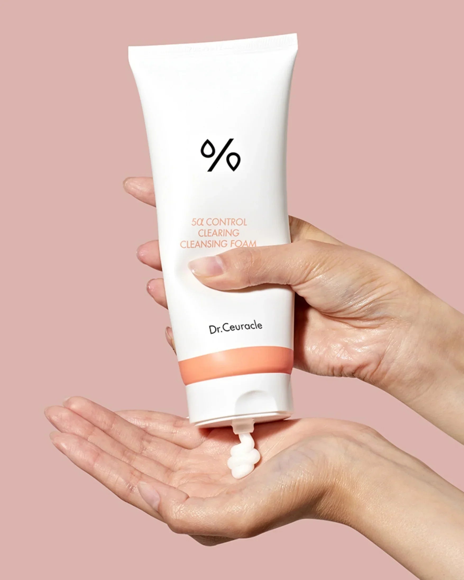 Hand squeezing Dr. Ceuracle 5α Control Clearing Cleansing Foam onto palm against pink background