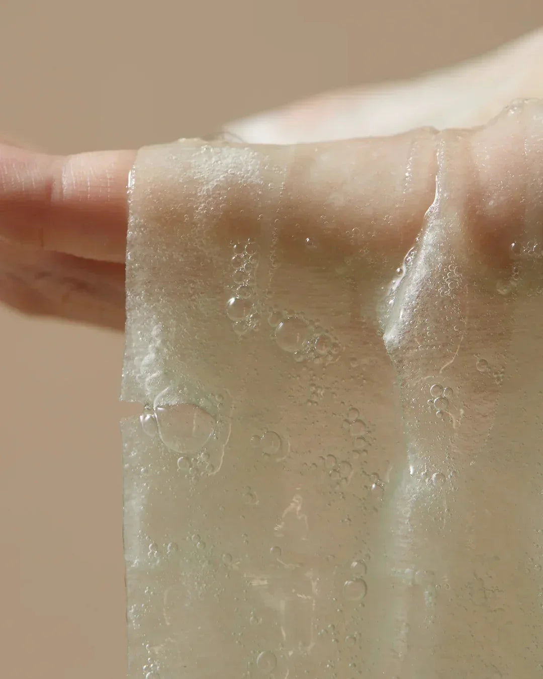 Hand holding a translucent sheet mask soaked in hydrating serum with bubbles
