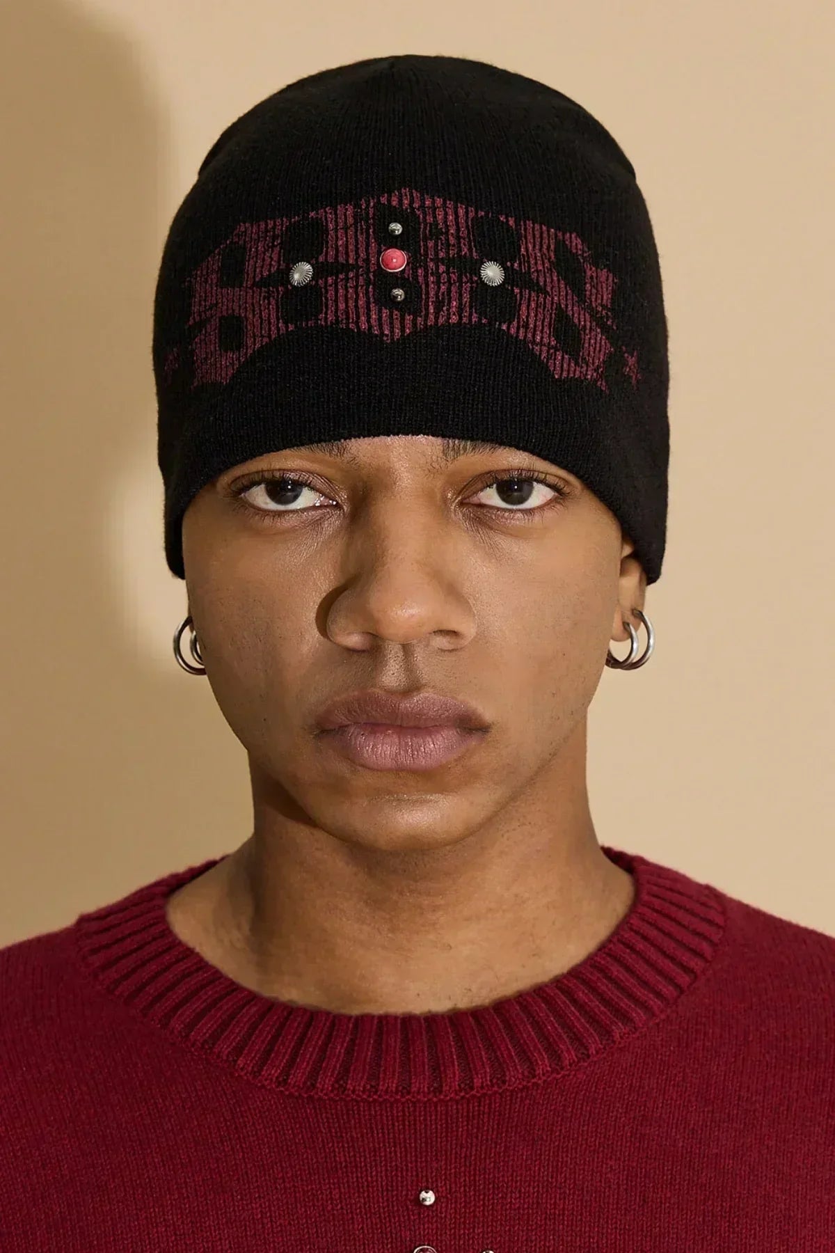 Close-up of man wearing black studded beanie with red design and red sweater with metal studs