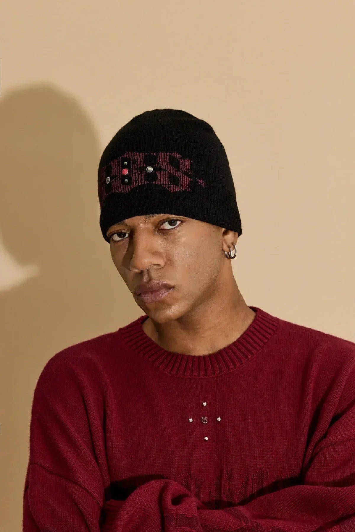 Man wearing black studded beanie and red sweater against beige background
