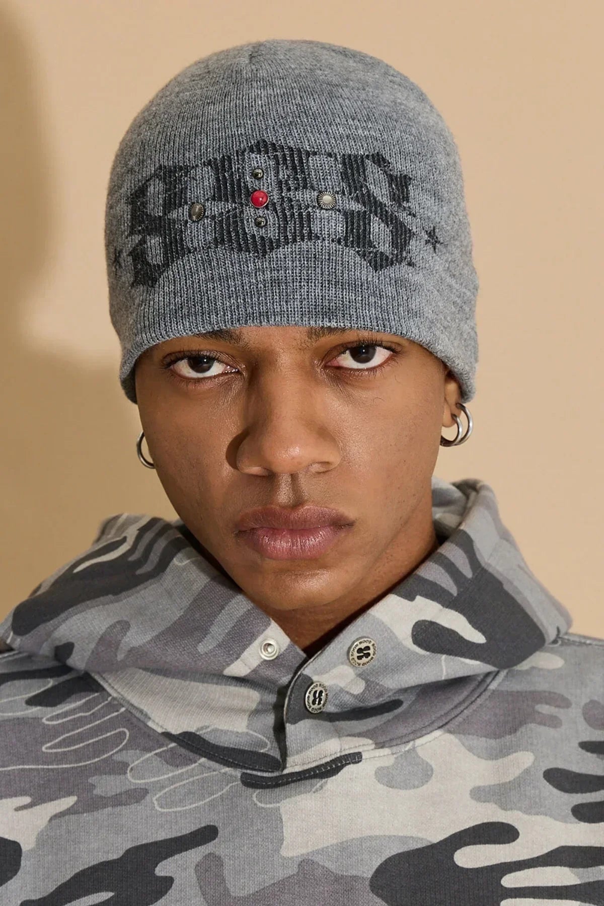 Close-up of a person wearing a grey studded beanie and grey camouflage hoodie