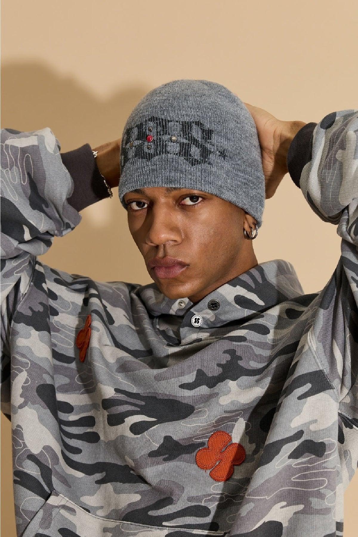 Man wearing grey studded beanie and grey camo hoodie with orange patches in studio
