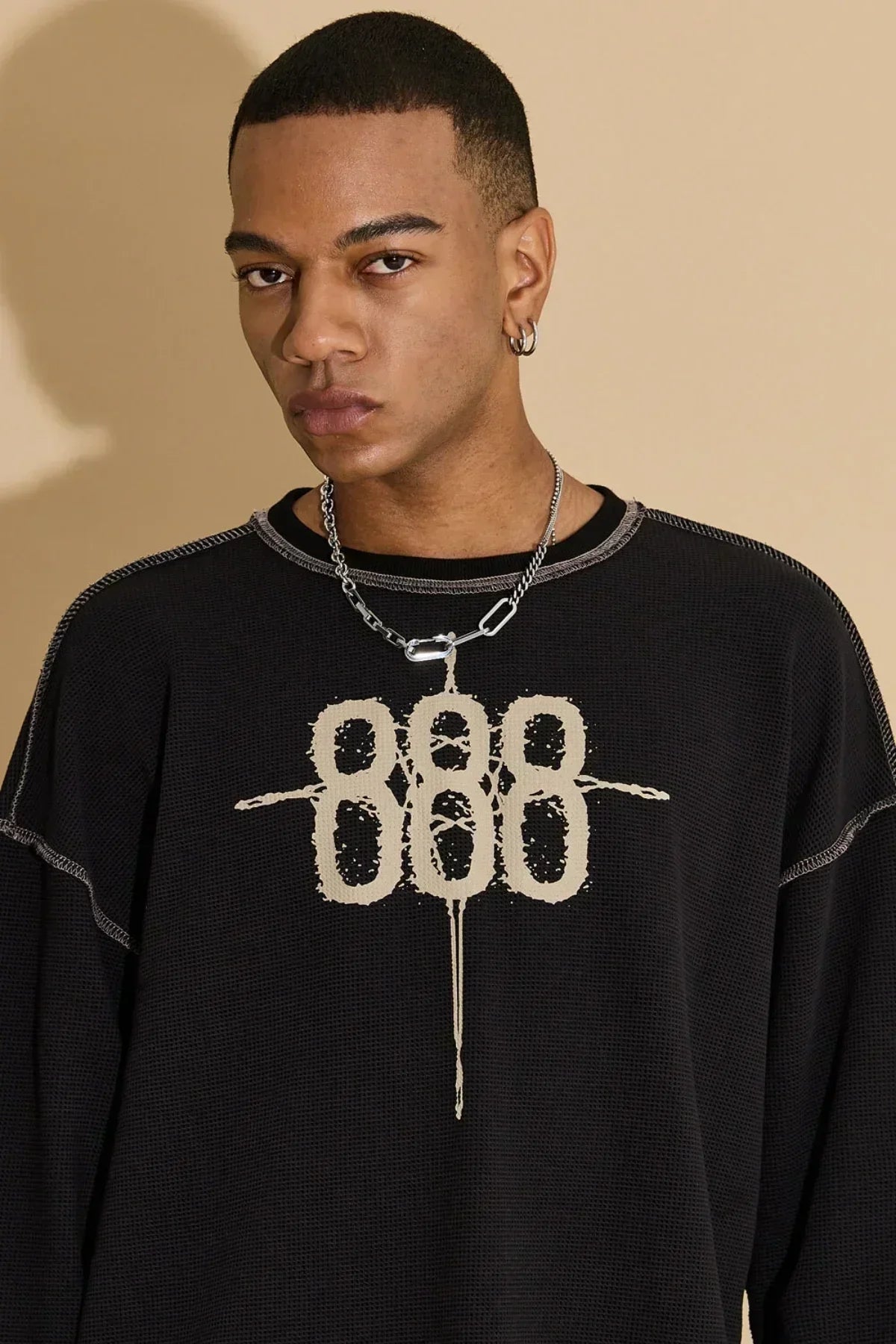 Close-up of a man wearing a black waffle knit long sleeve T-shirt with beige 888 graphic and silver chain necklace