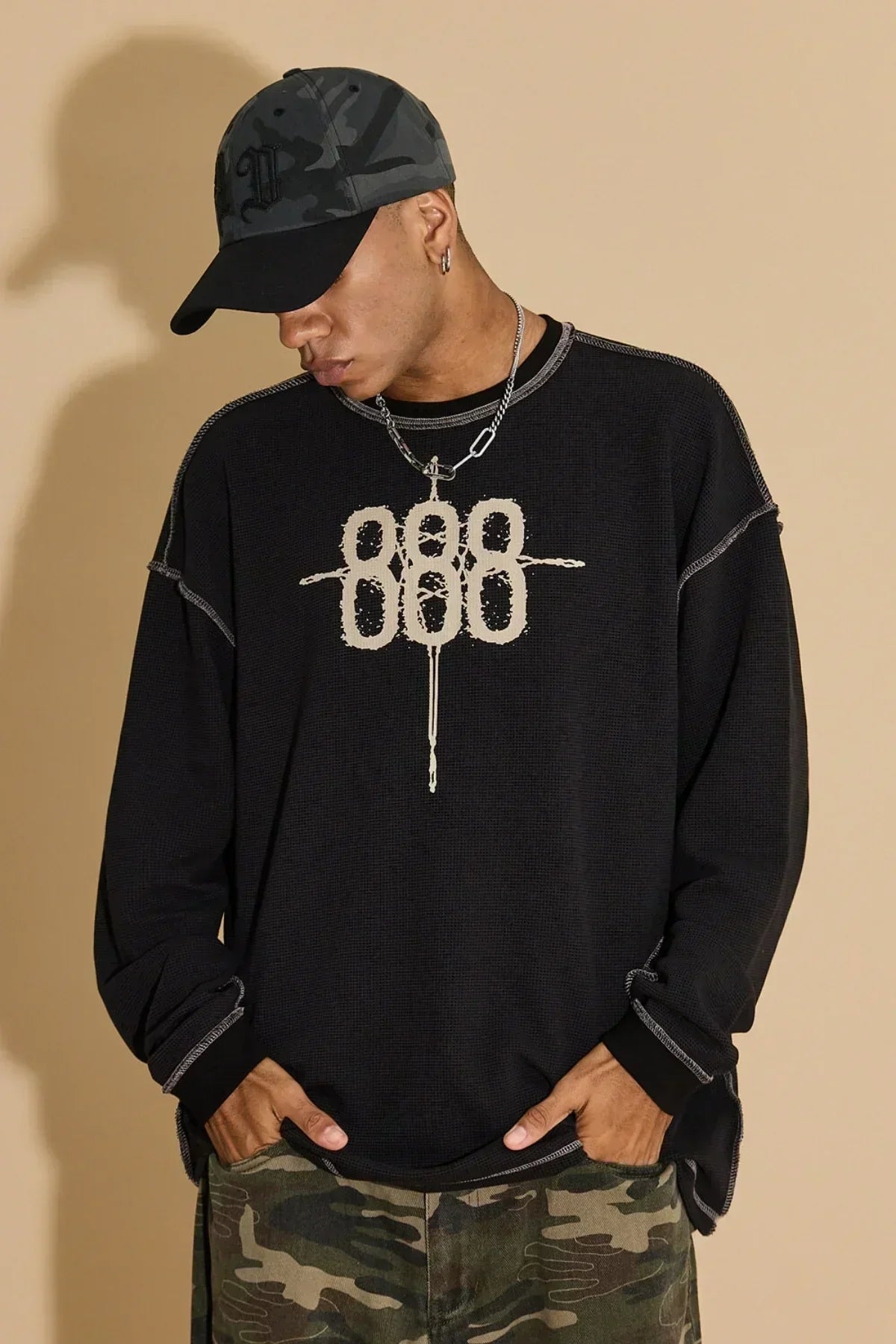 Man wearing black waffle long sleeve t-shirt with 888 graphic, camo pants, and camo black cap
