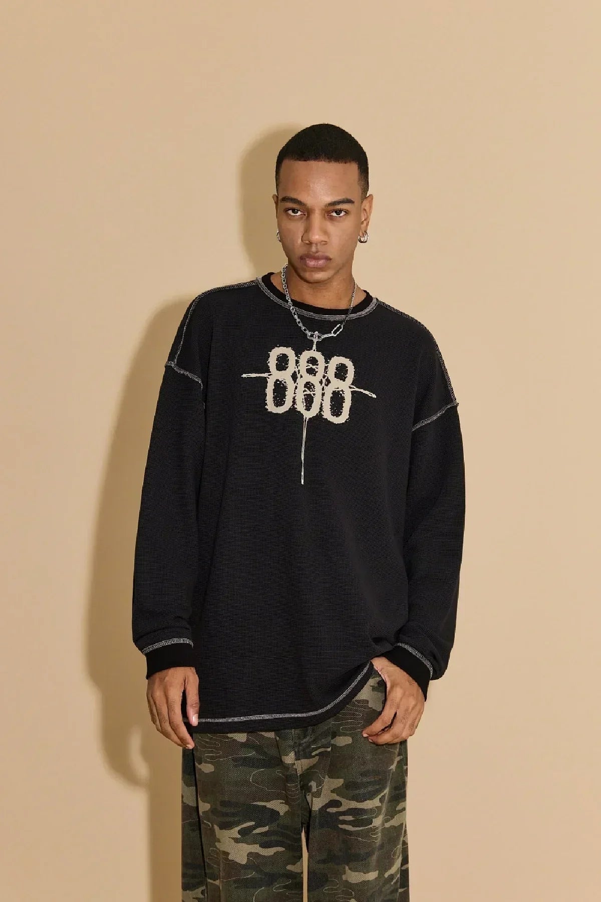 Model wearing black waffle long sleeve t-shirt with 888 logo and camo pants against beige background