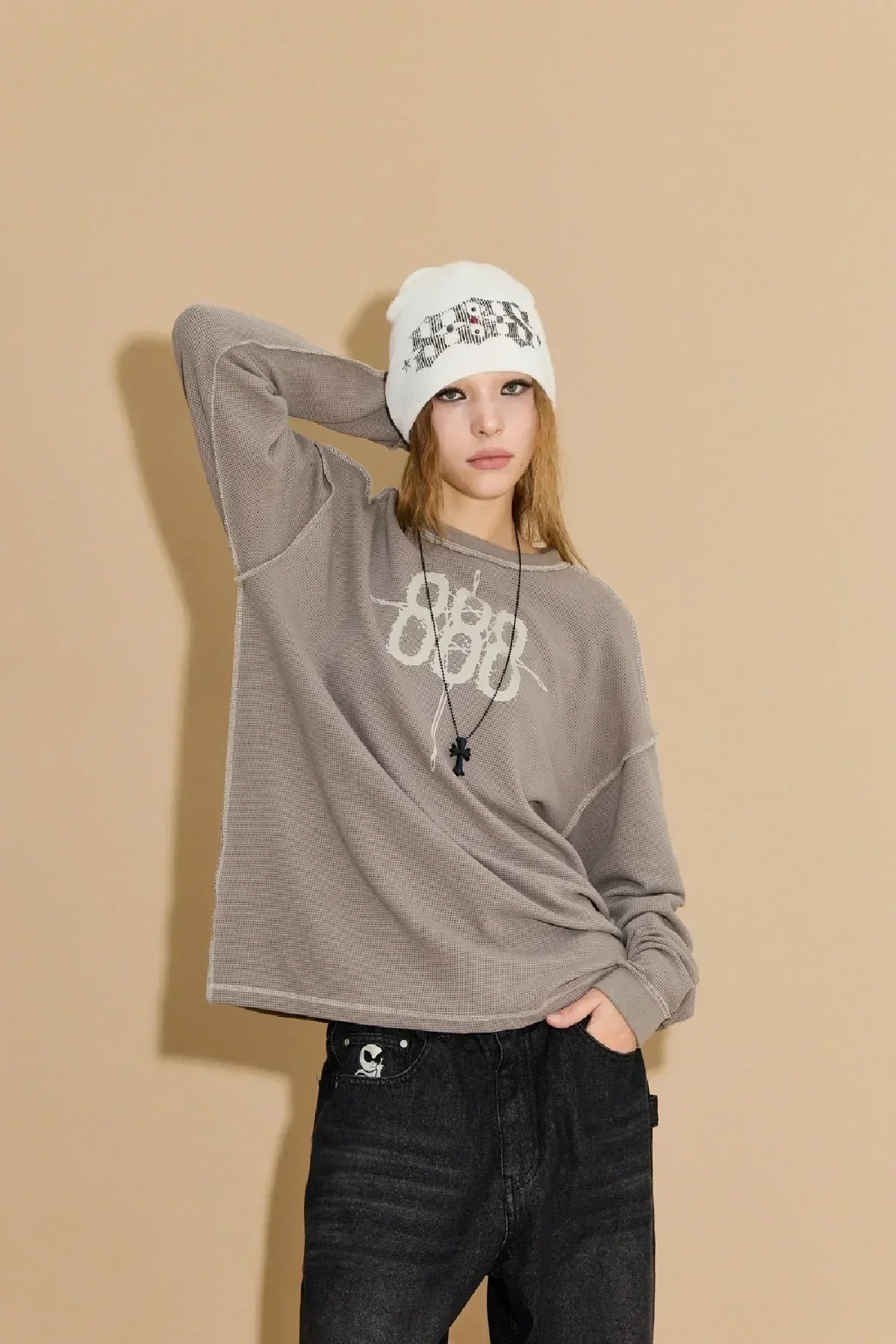 Model wearing beige waffle long sleeve T-shirt with 888 print and white beanie against beige backdrop