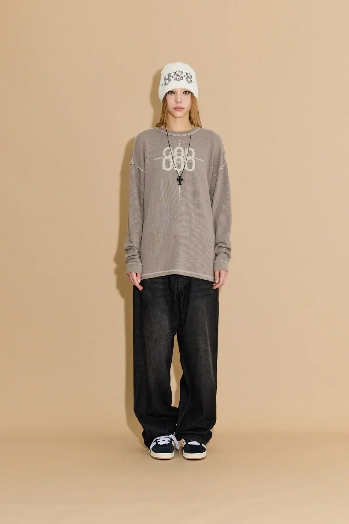 Model wearing greyish beige waffle long sleeve shirt with 888 print, black baggy jeans, white beanie, and sneakers