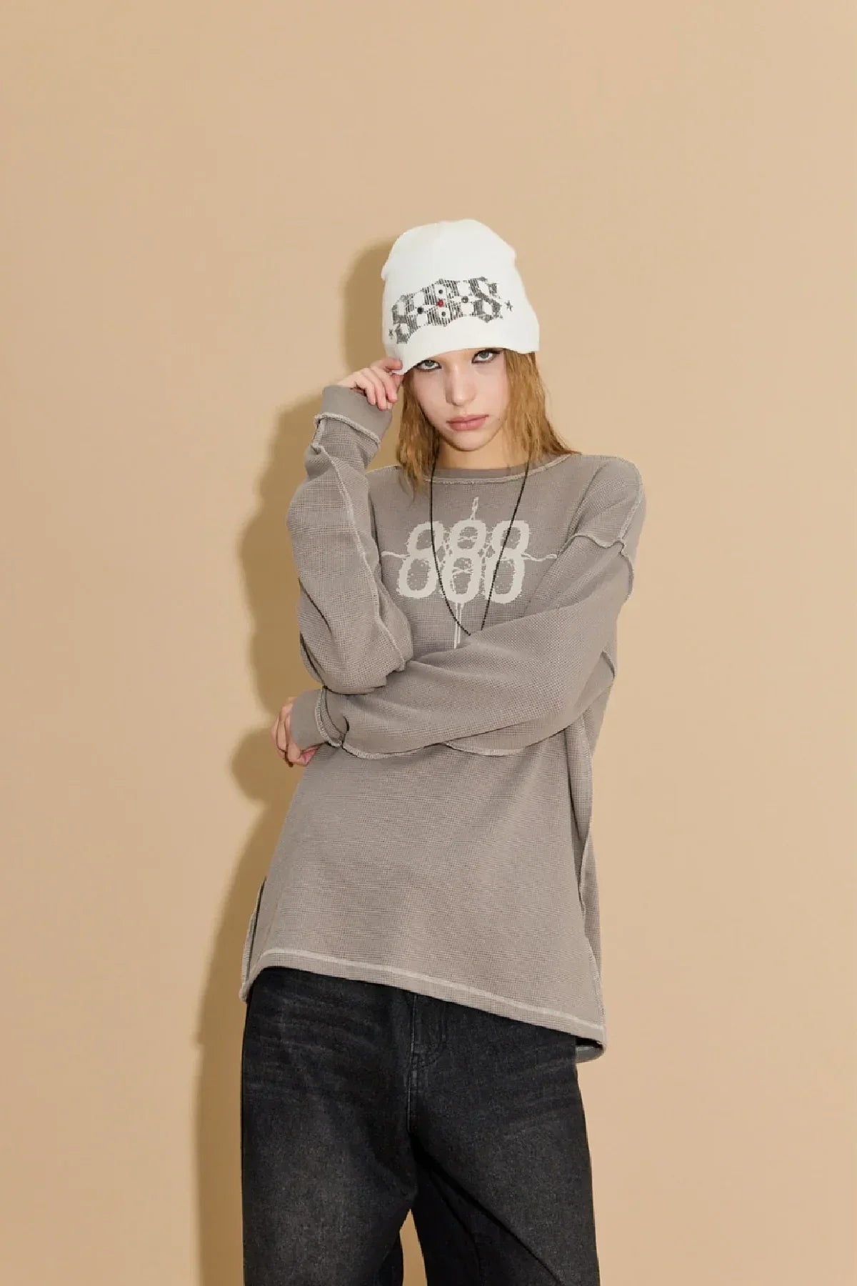 Model wearing greyish beige waffle long sleeve shirt with 888 design and white beanie hat