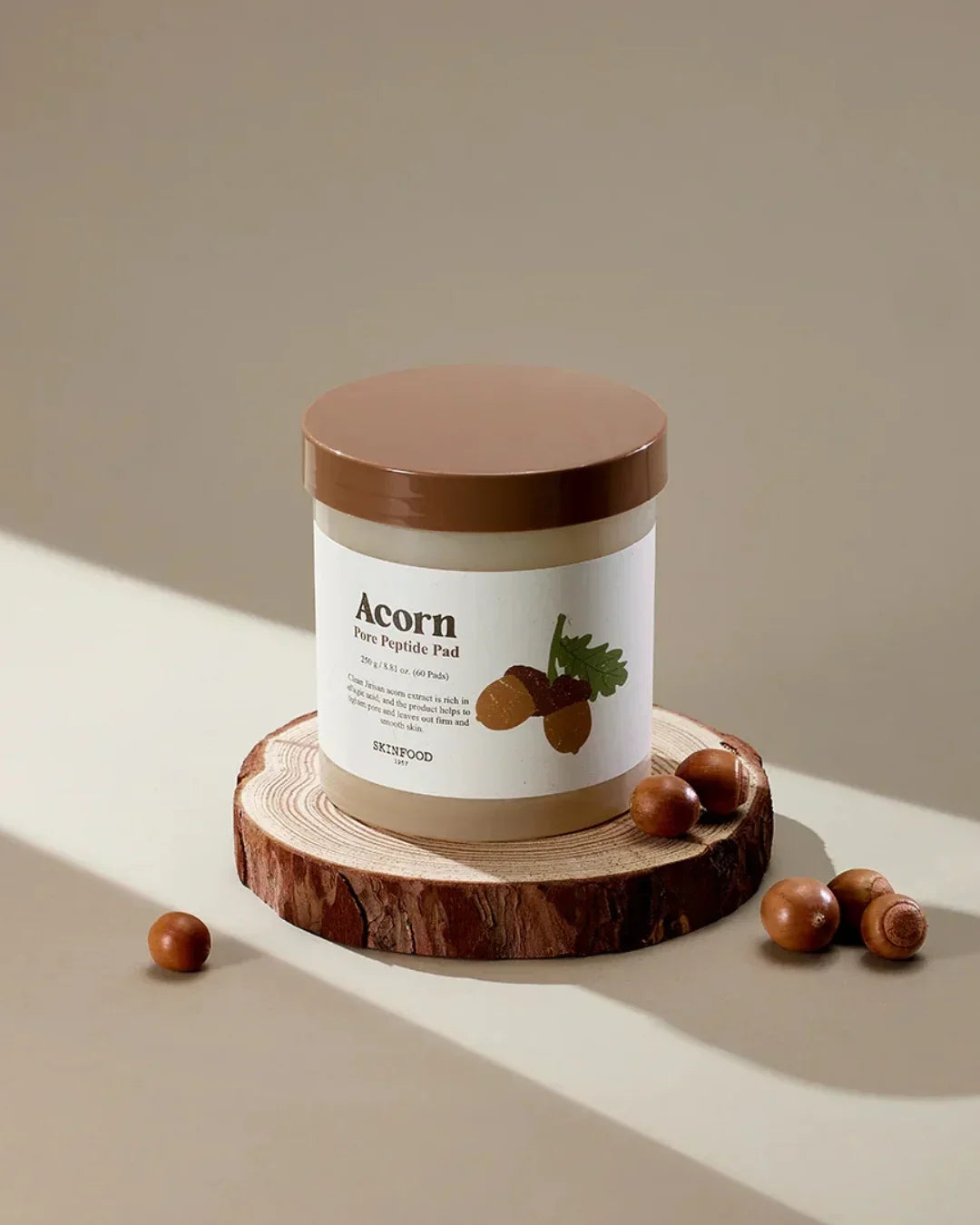 Skinfood Acorn Pore Peptide Pad jar on wooden slice with acorns on beige background