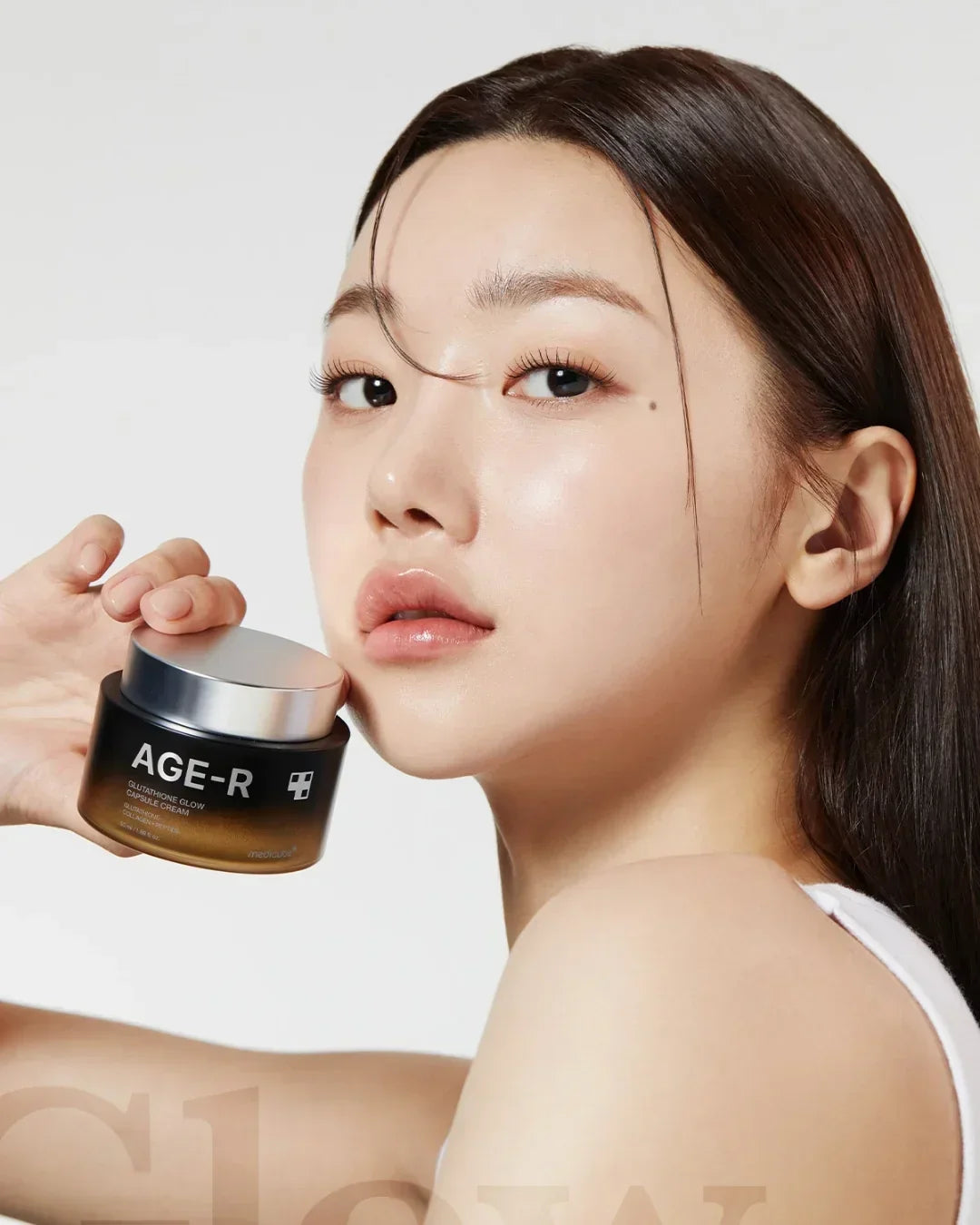 Woman with glowing skin holding AGE-R Glutathione Glow Capsule Cream jar, skincare product