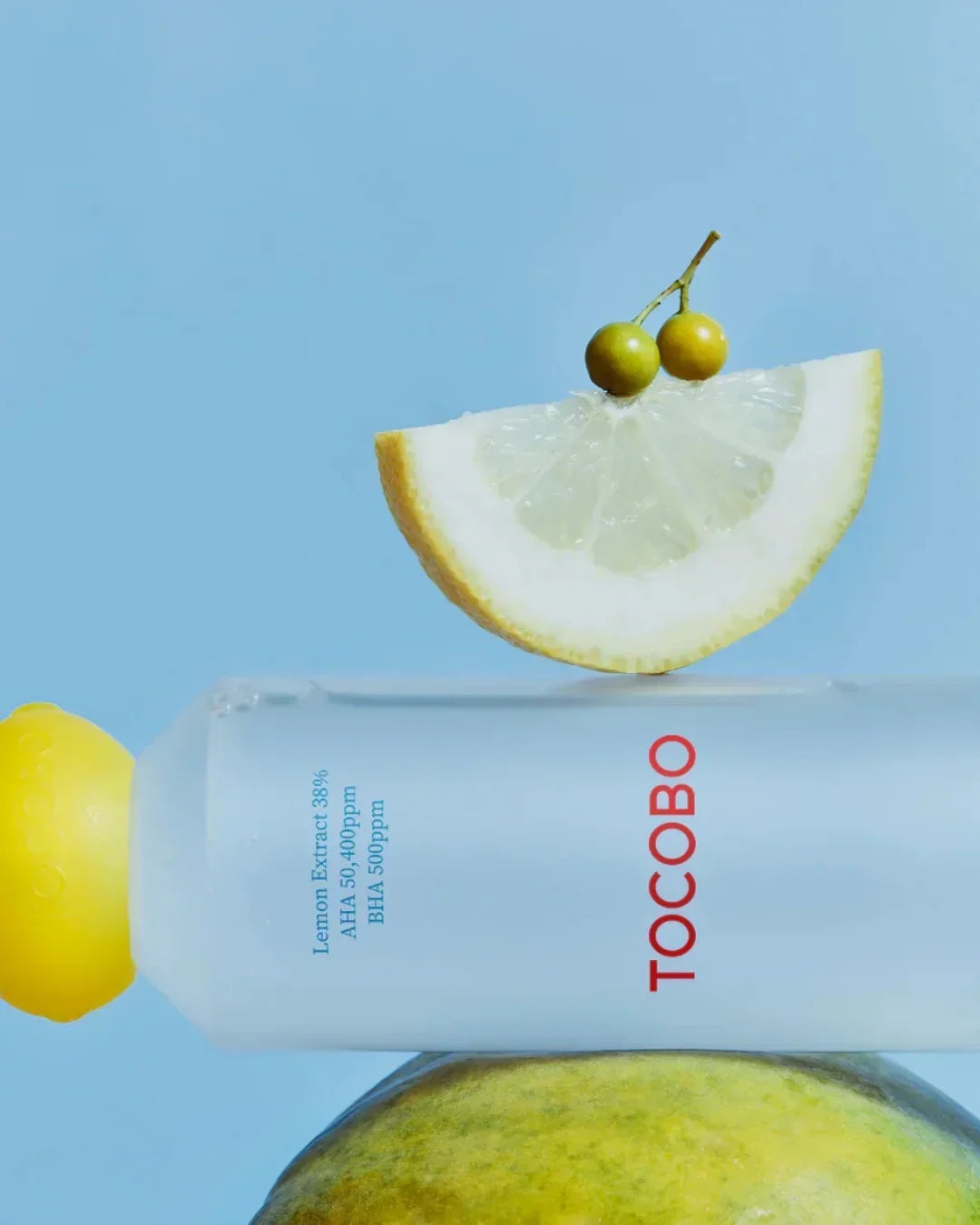 Tocobo lemon toner bottle with lemon slice and small berries on blue background