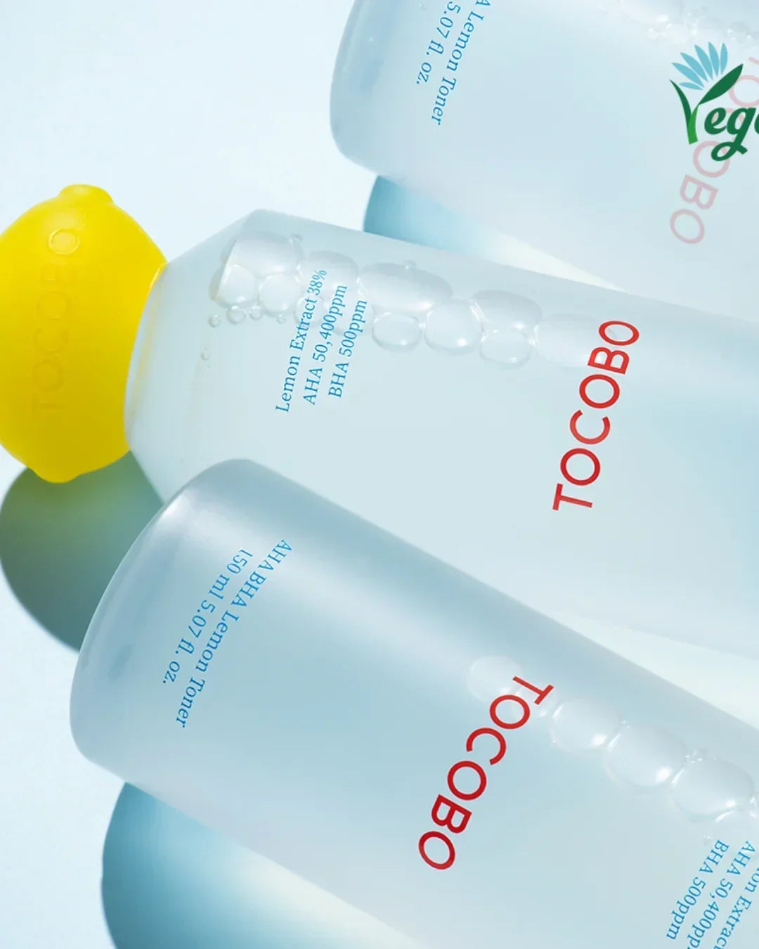 Three TOCOBO AHA BHA Lemon Toner bottles with water droplets and a yellow lemon-shaped cap on a light background