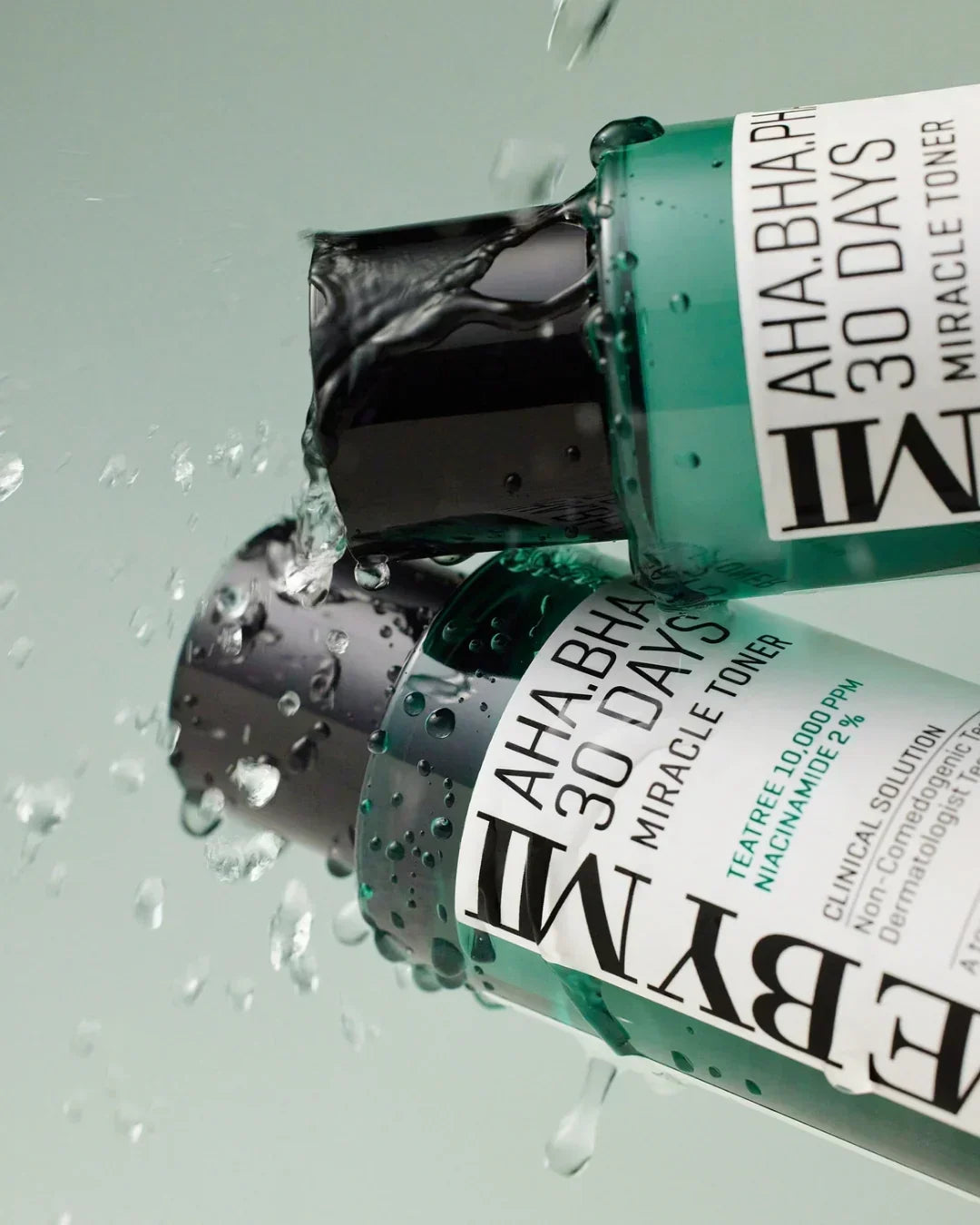 Close-up of ESYME AHA BHA PHA 30 Days Miracle Toner bottles with water splash on green background
