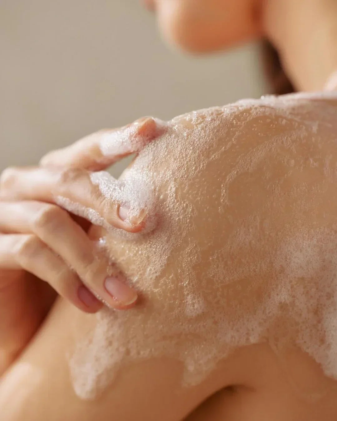 Close-up of a person applying foamy body cleanser foam on shoulder