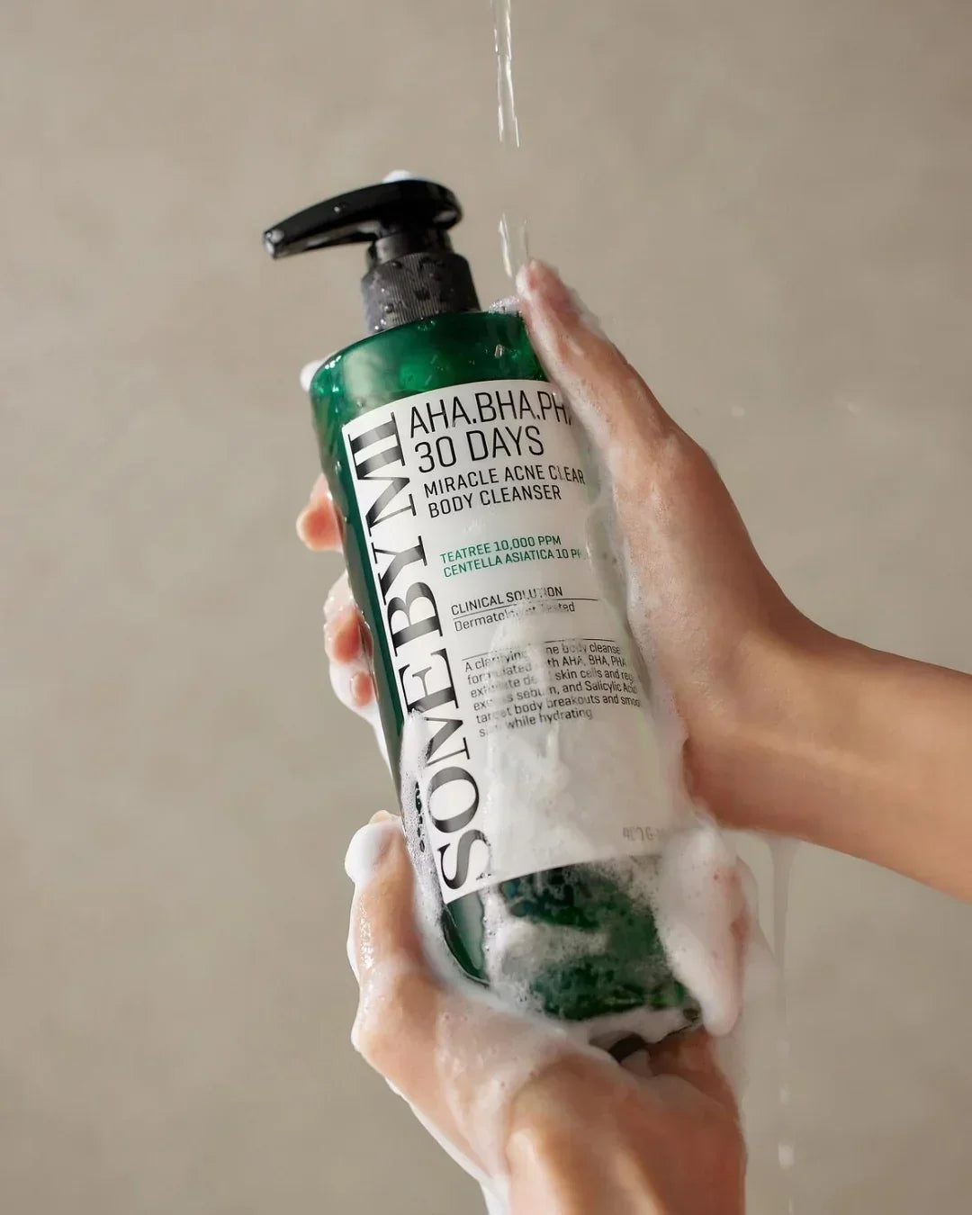 Hands holding green SONEBYNT 30 Days Miracle Acne Clear Body Cleanser bottle with foam