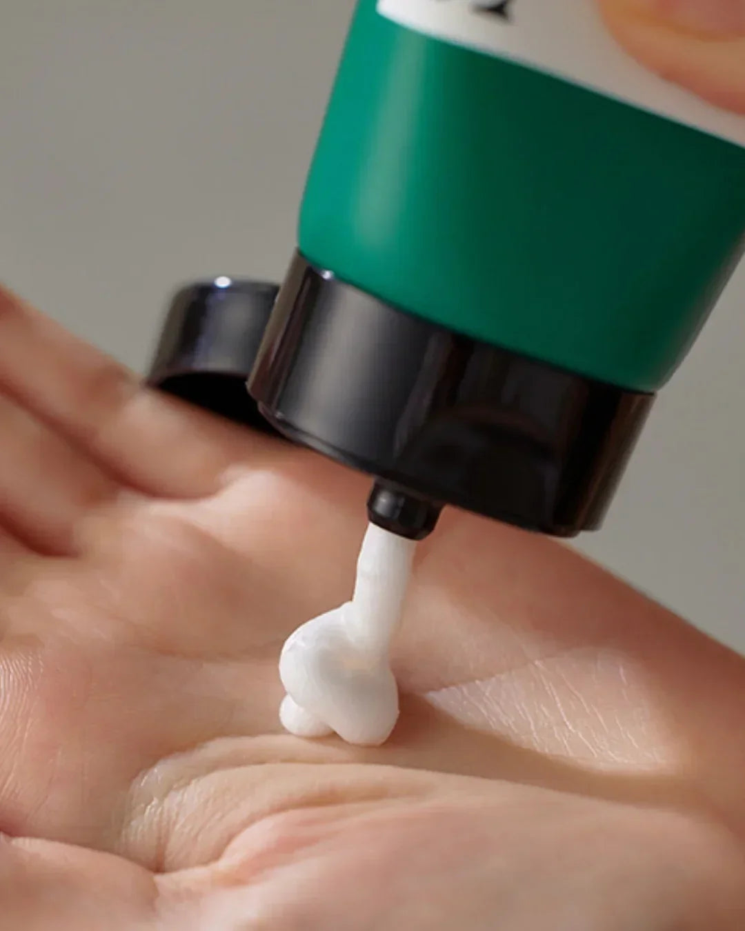 Close-up of skincare foam being dispensed from a green tube onto a person's palm