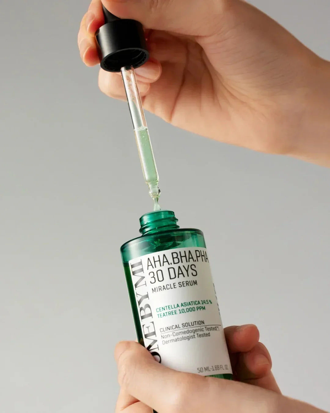 Close-up of hands holding a green bottle and dropper of AHA BHA PHA 30 Days Miracle Serum skincare product