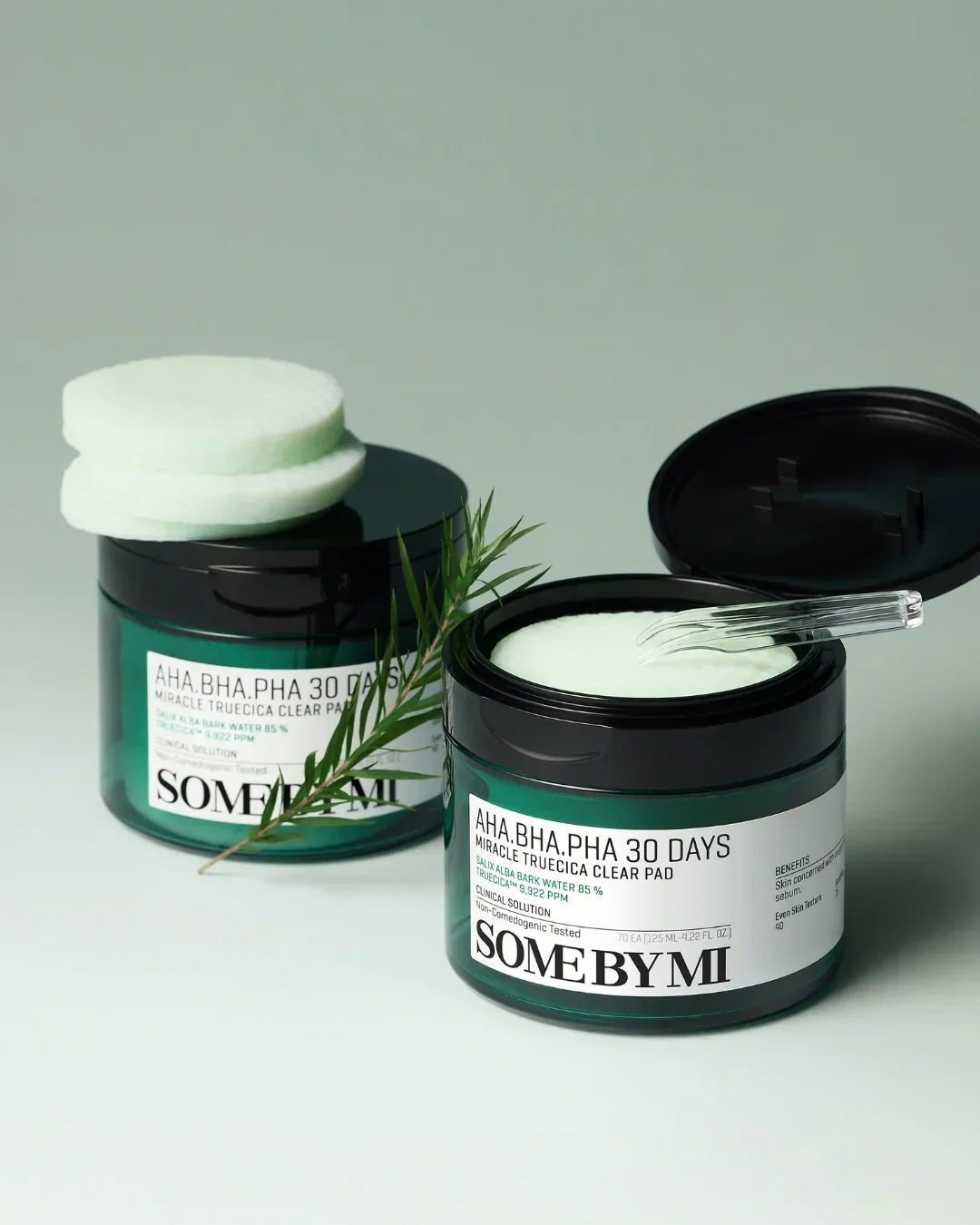 Two green jars of SOME BY MI AHA BHA PHA 30 Days Miracle Truecica Clear Pads with cotton pads and a green leaf