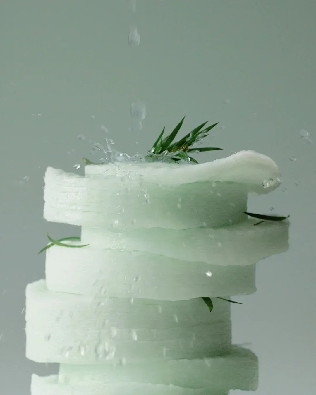 Stack of white melon slices with green leaves and water droplets on a light gray background